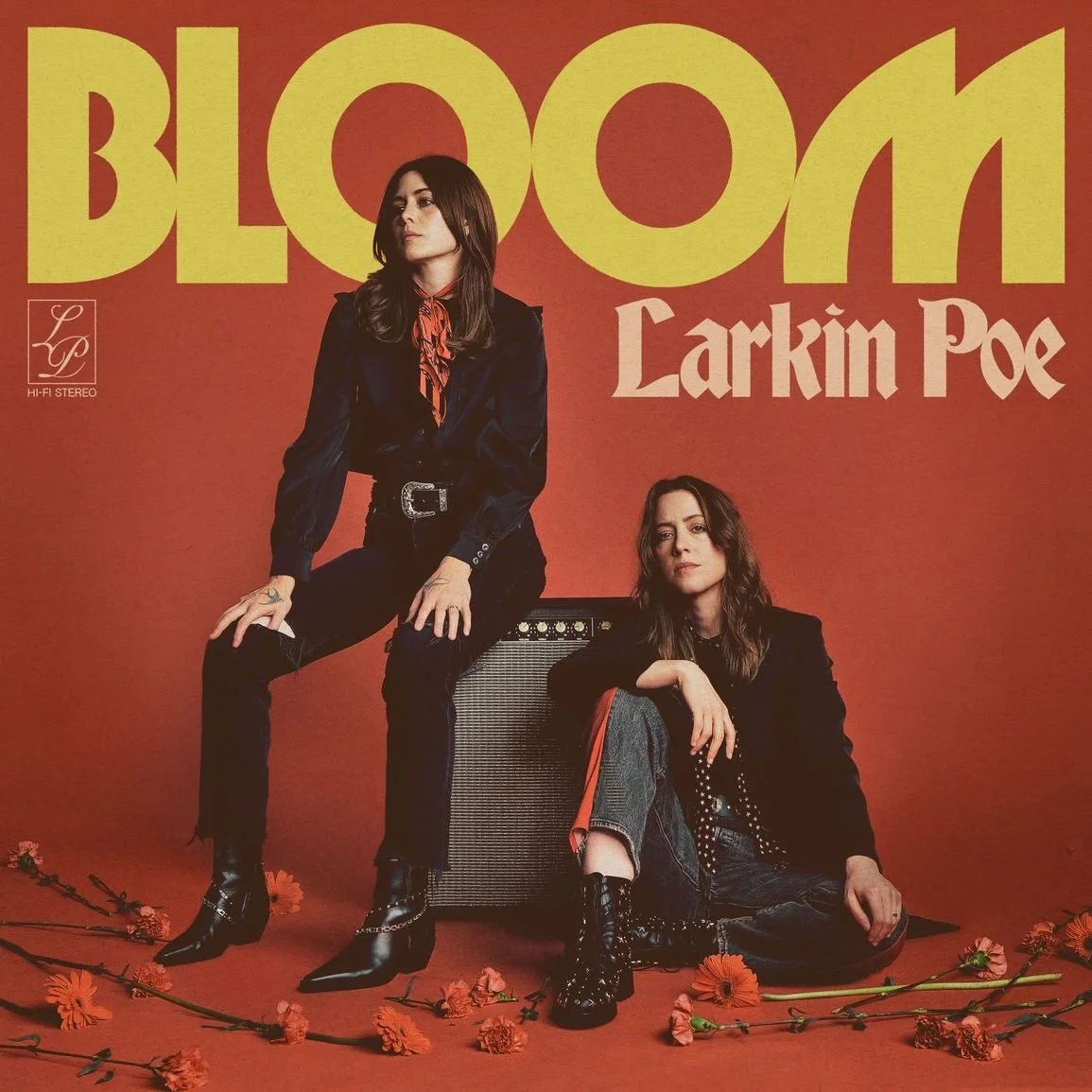 Das Cover eines Albums oder Posters mit den Titeln "BLOOM" und "Larkin Poe". Zwei Frauen sitzen vor einem roten Hintergrund, eine auf einem Verstärker, die andere auf dem Boden. Es liegen mehrere Blumen auf dem Boden, und beide Frauen tragen dunkle Kleidung.