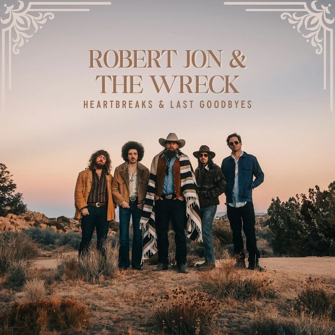 Das Bild zeigt die Band 'Robert Jon & The Wreck' im Freien bei Sonnenuntergang in einer Wüstenlandschaft, mit fünf Männern in Western- und Boho-Kleidung.