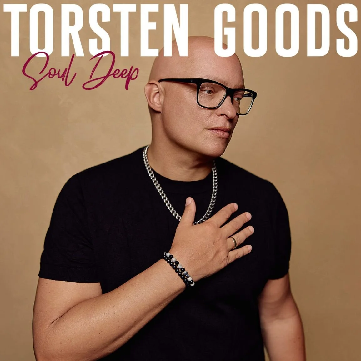 Albumcover mit einem Mann, der eine schwarze Brille trägt, schwarzen T-Shirt, eine silberne Kette, Armbänder und eine Hand auf der Brust, vor einem beigefarbenen Hintergrund. Über dem Bild ist der Schriftzug 'Torsten Goods Soul Deep'.