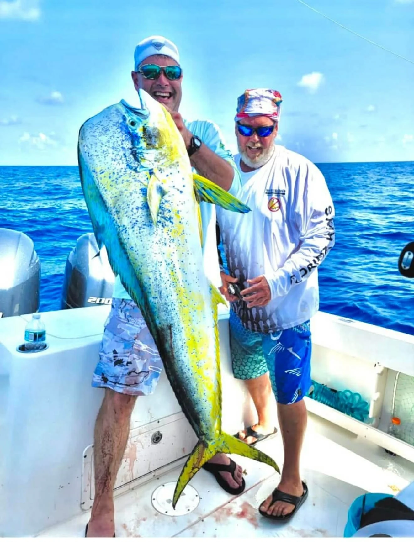 Two men on a boat holding a large yellow and blue fish they caught while fishing in the ocean.
