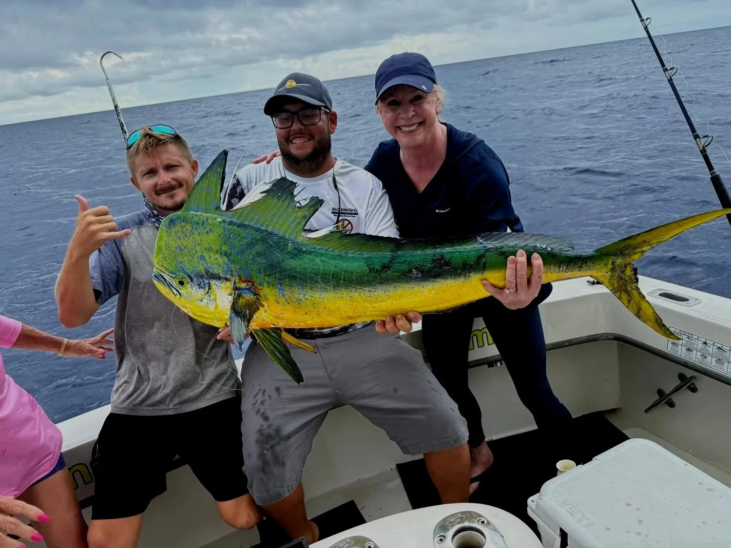 Three people on a boat holding a large sailfish, with the ocean and cloudy sky in the background.