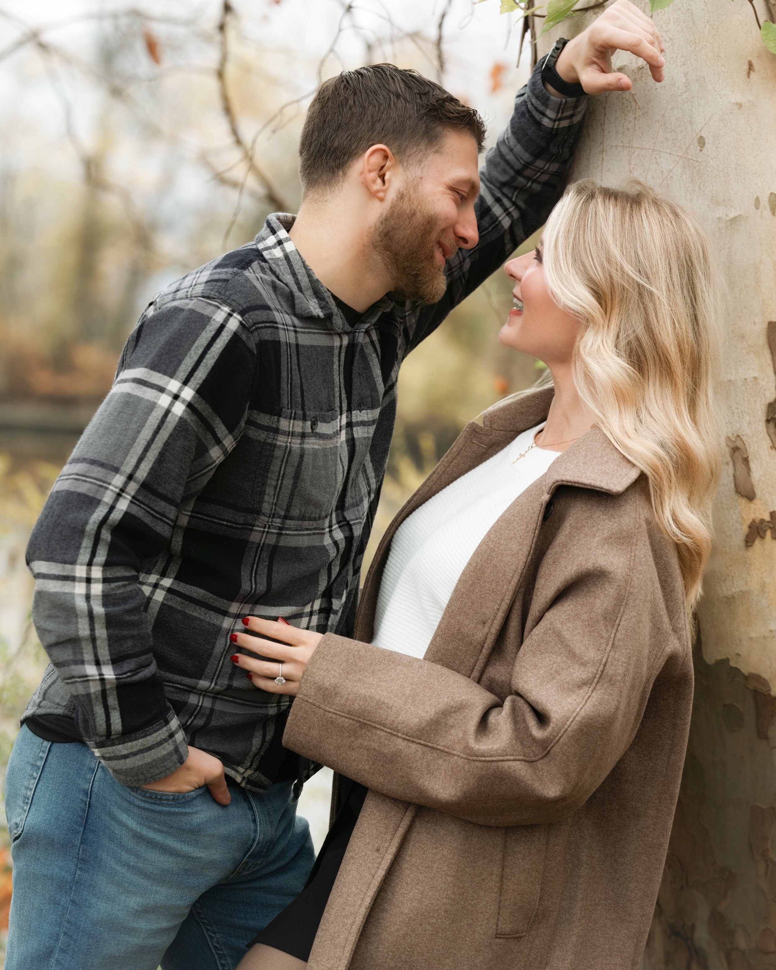 A couple outdoors, close together, smiling and looking into each other's eyes during autumn.