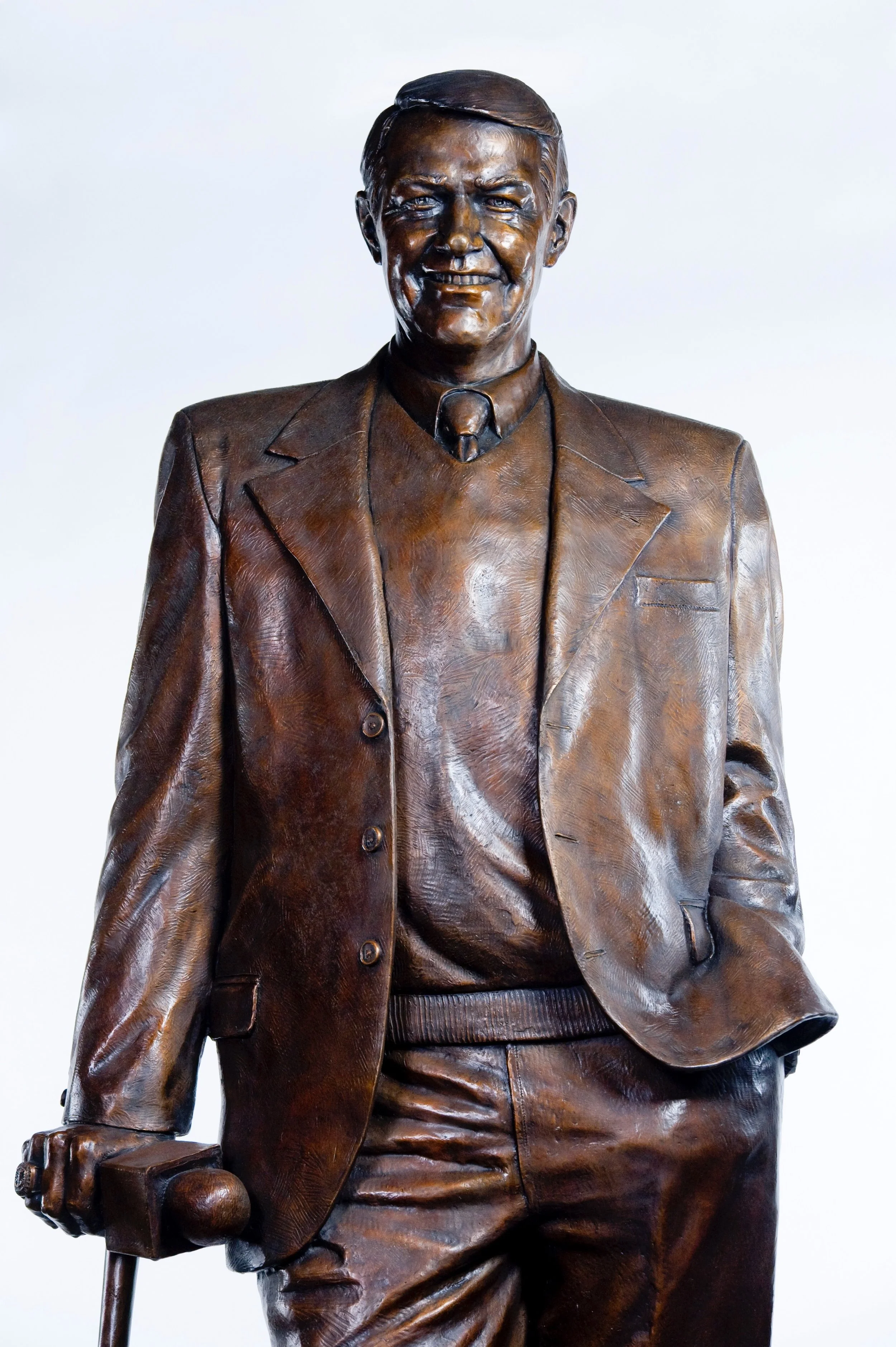 A bronze statue of a man in a suit and tie, smiling, with his right hand resting on a cane.