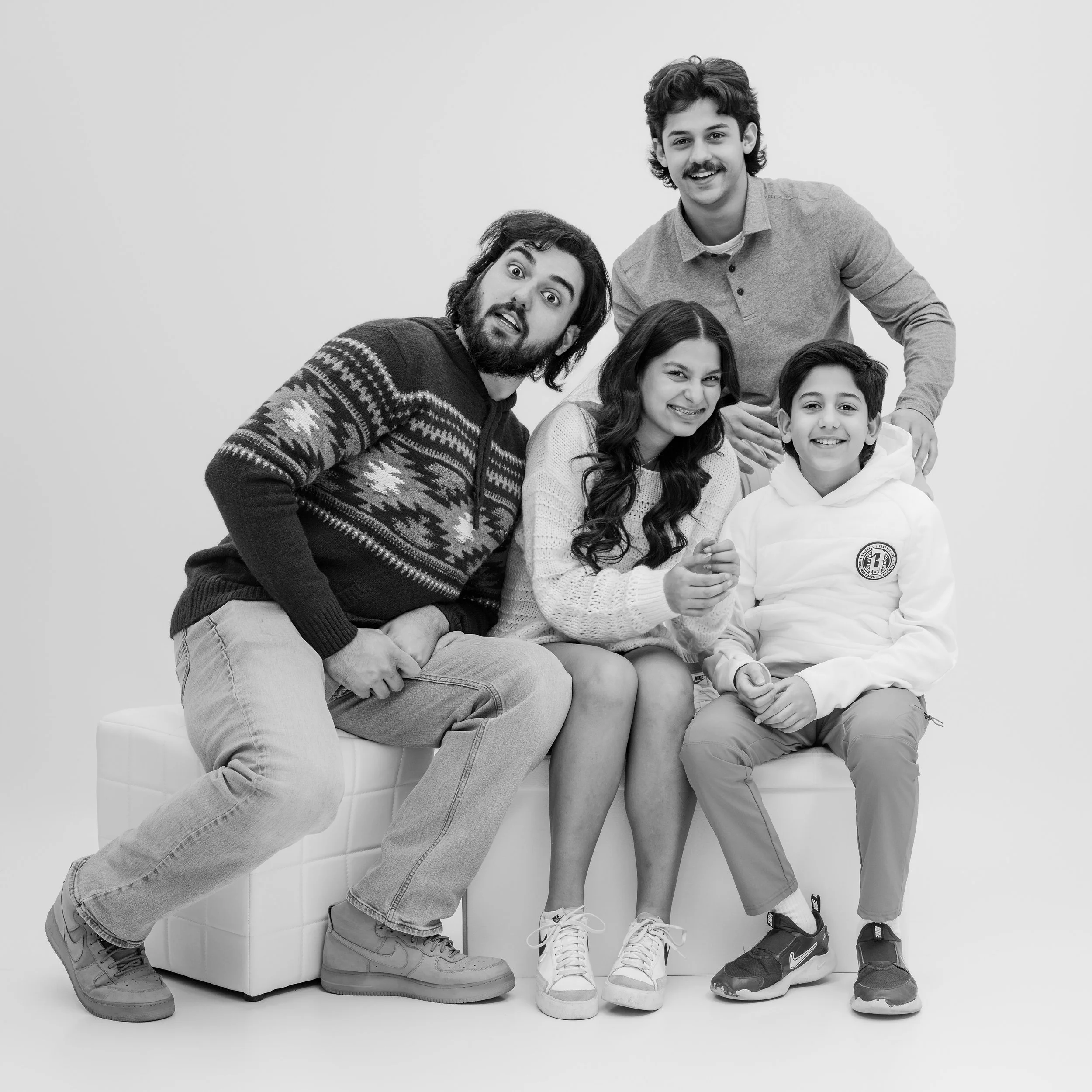 Black and white photo of five people, two adults and three children, posing together for a group photo against a plain background. The adults are seated on a bench while the children stand behind them, all smiling and looking at the camera.
