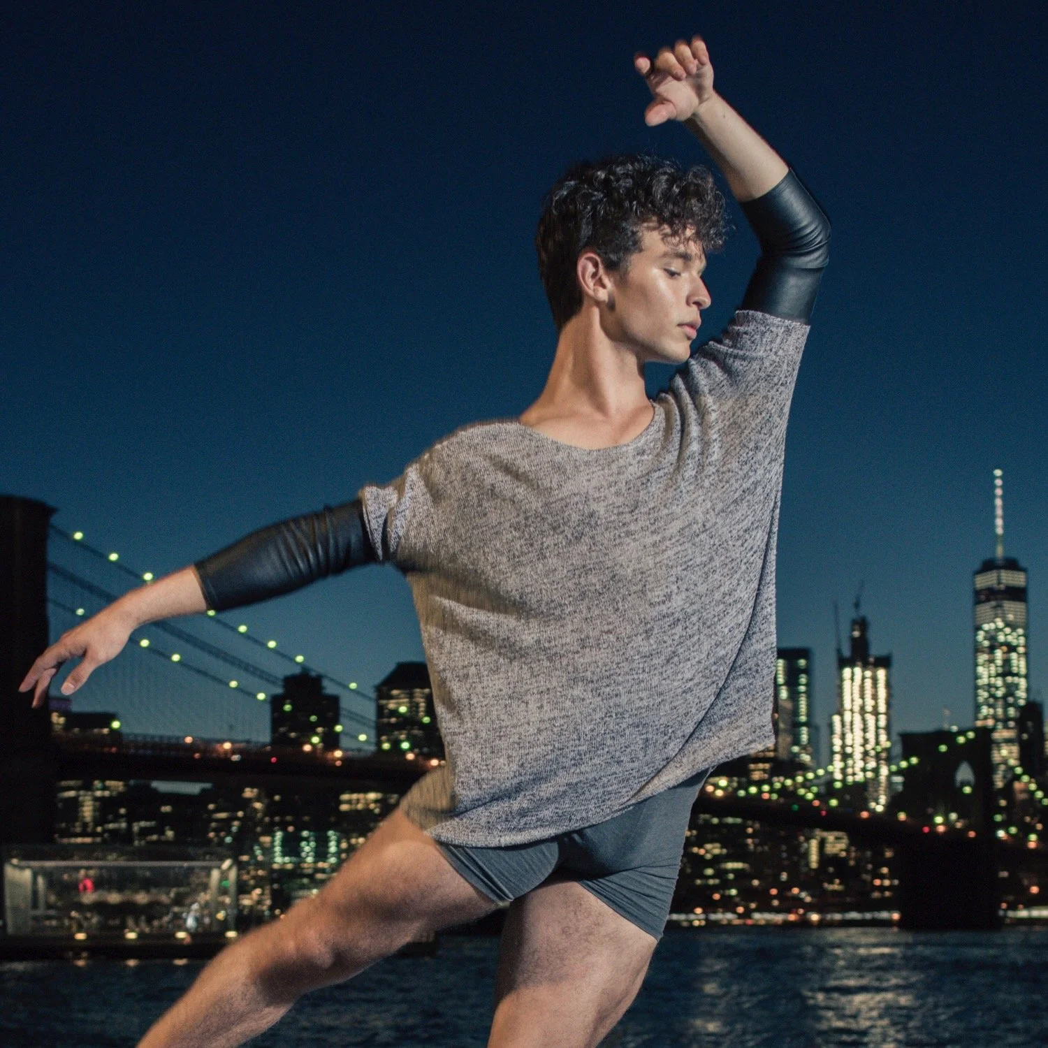 A person dancing outdoors at night, with a city skyline and bridge in the background.