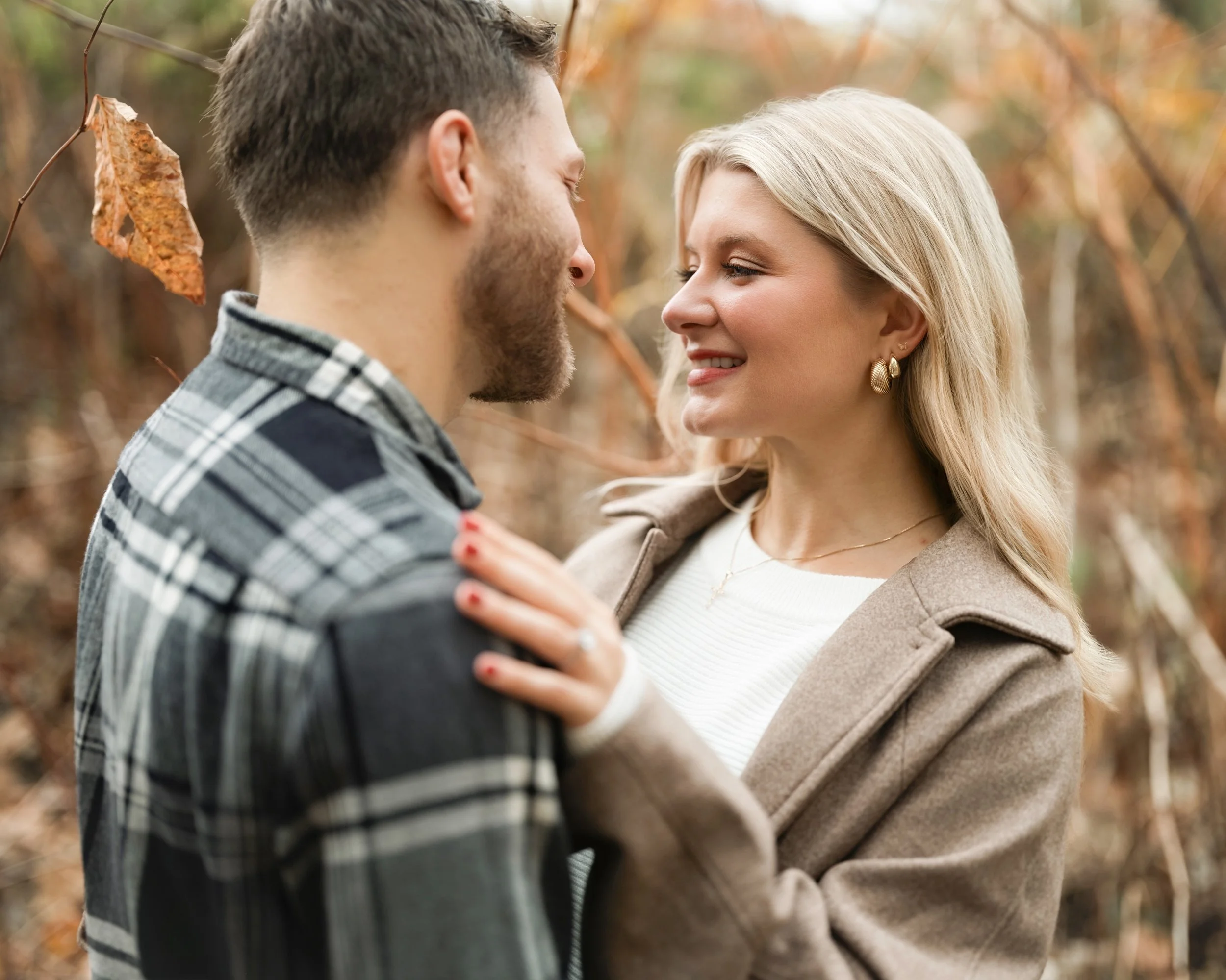A couple in an embrace outdoors during fall, smiling at each other.