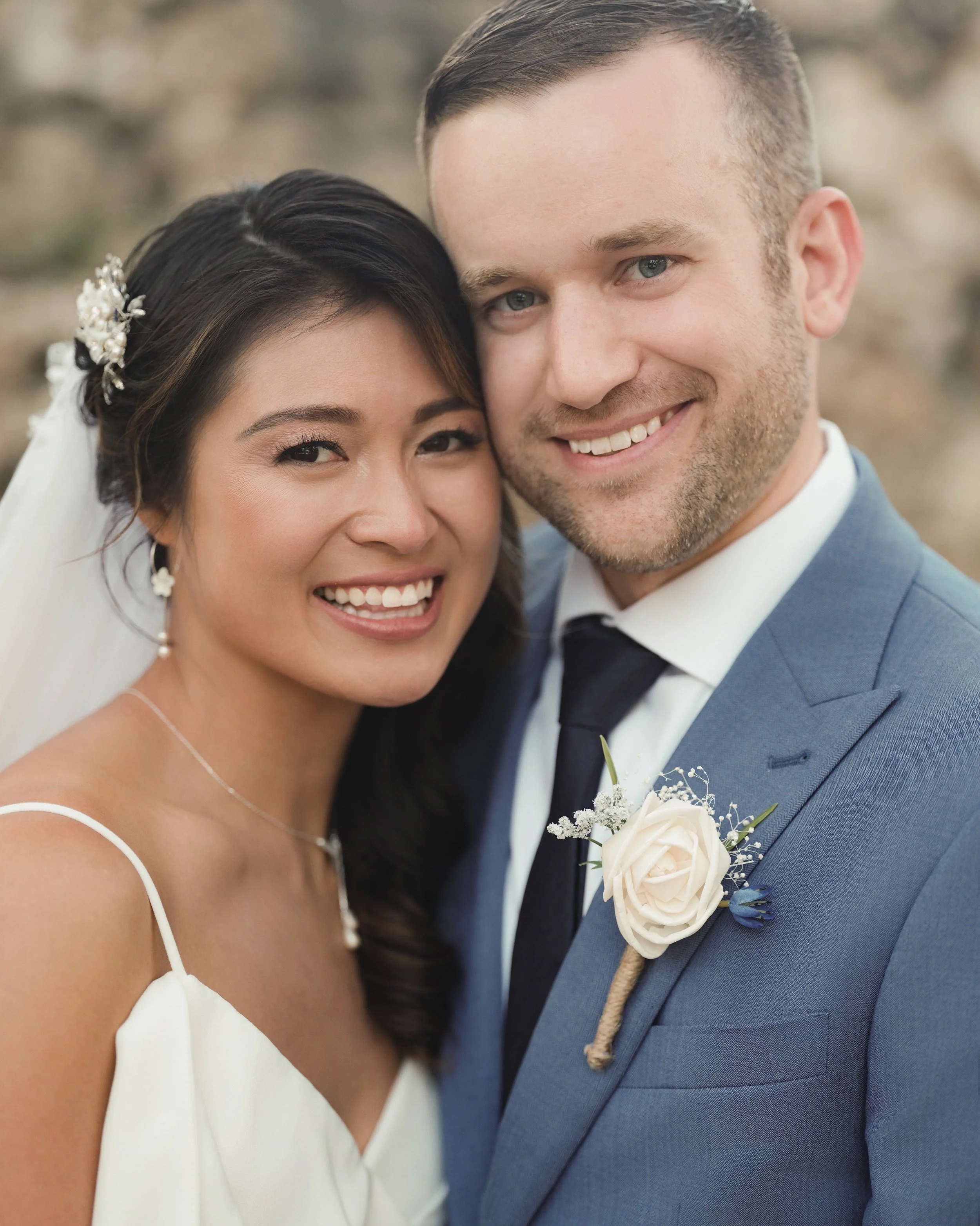 Smiling bride and groom in wedding attire, close-up portrait, outdoors.