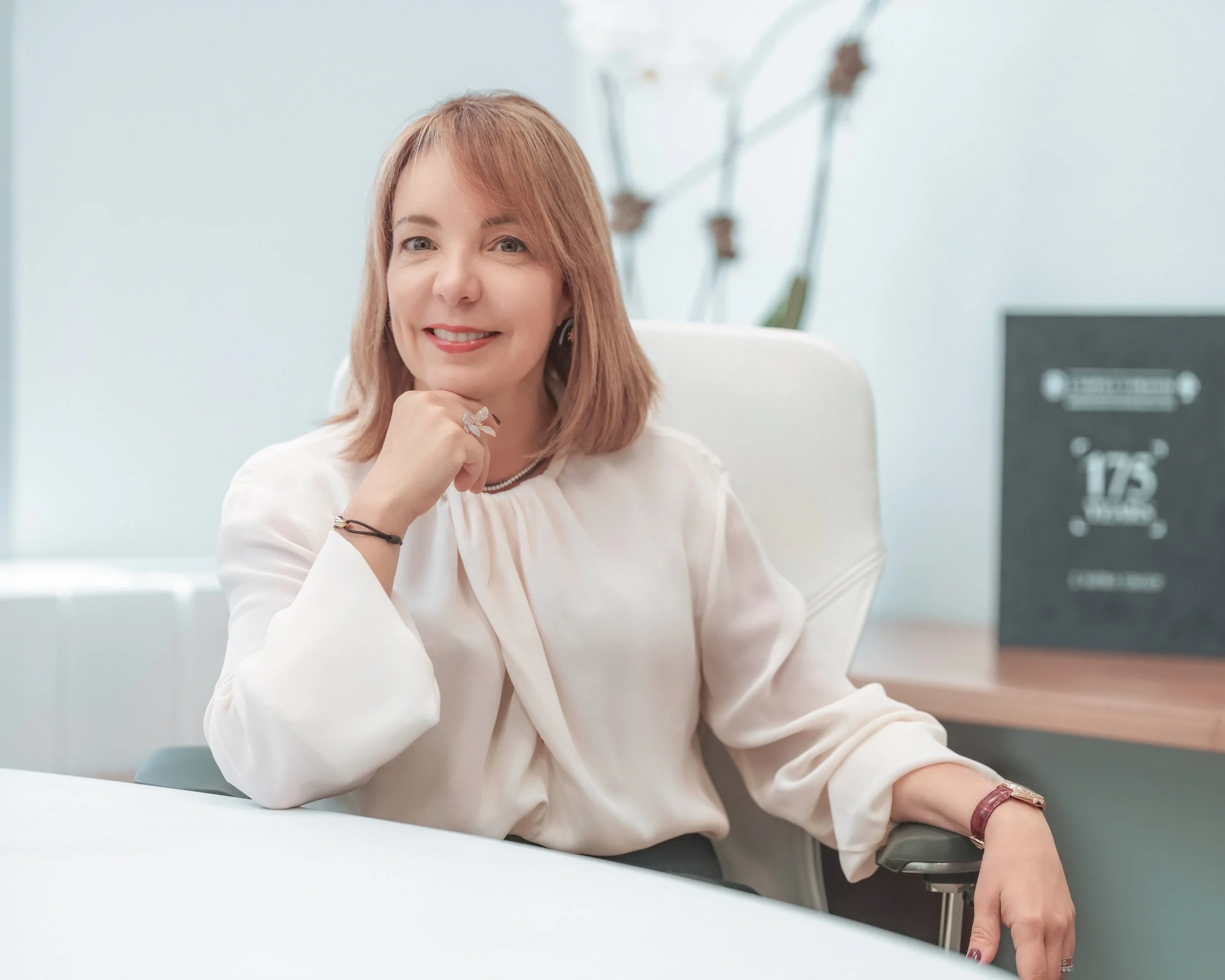 Smiling woman with blonde hair sitting at a desk in an office.