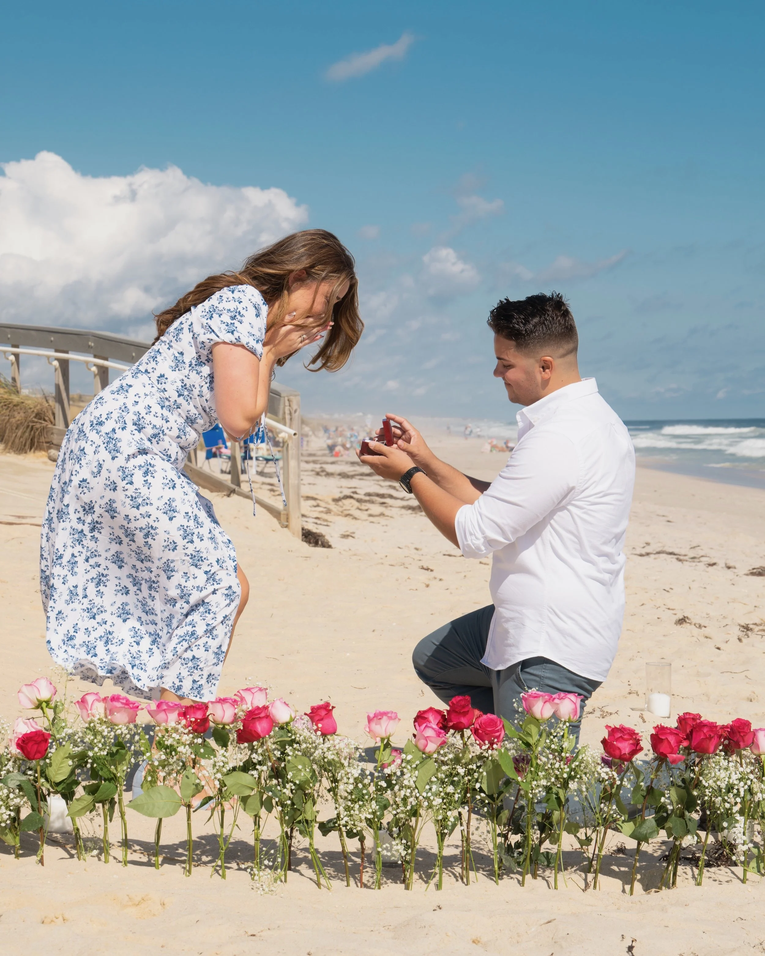 A man proposing to a woman on the beach, surrounded by pink and white roses.