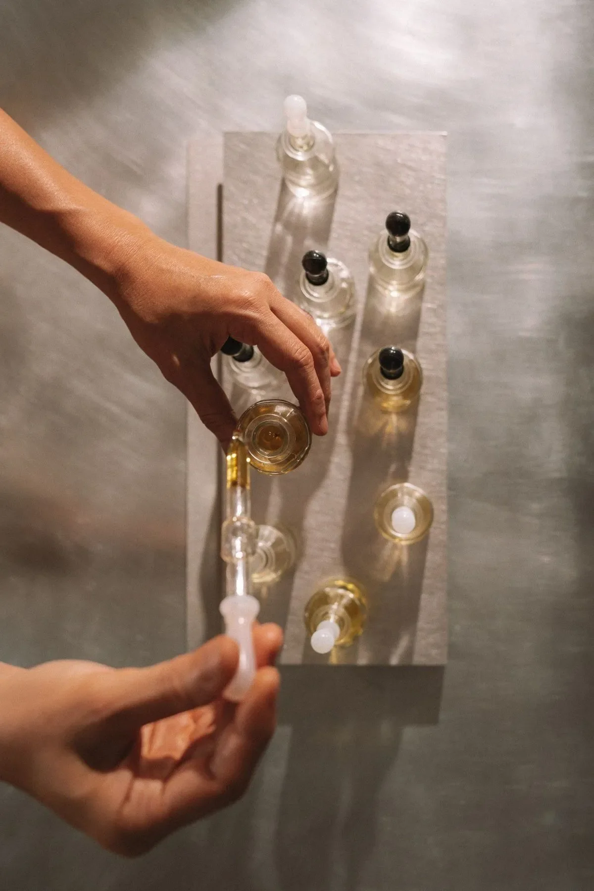 Person filling a small glass pipette with a yellow liquid from a glass dropper bottle.