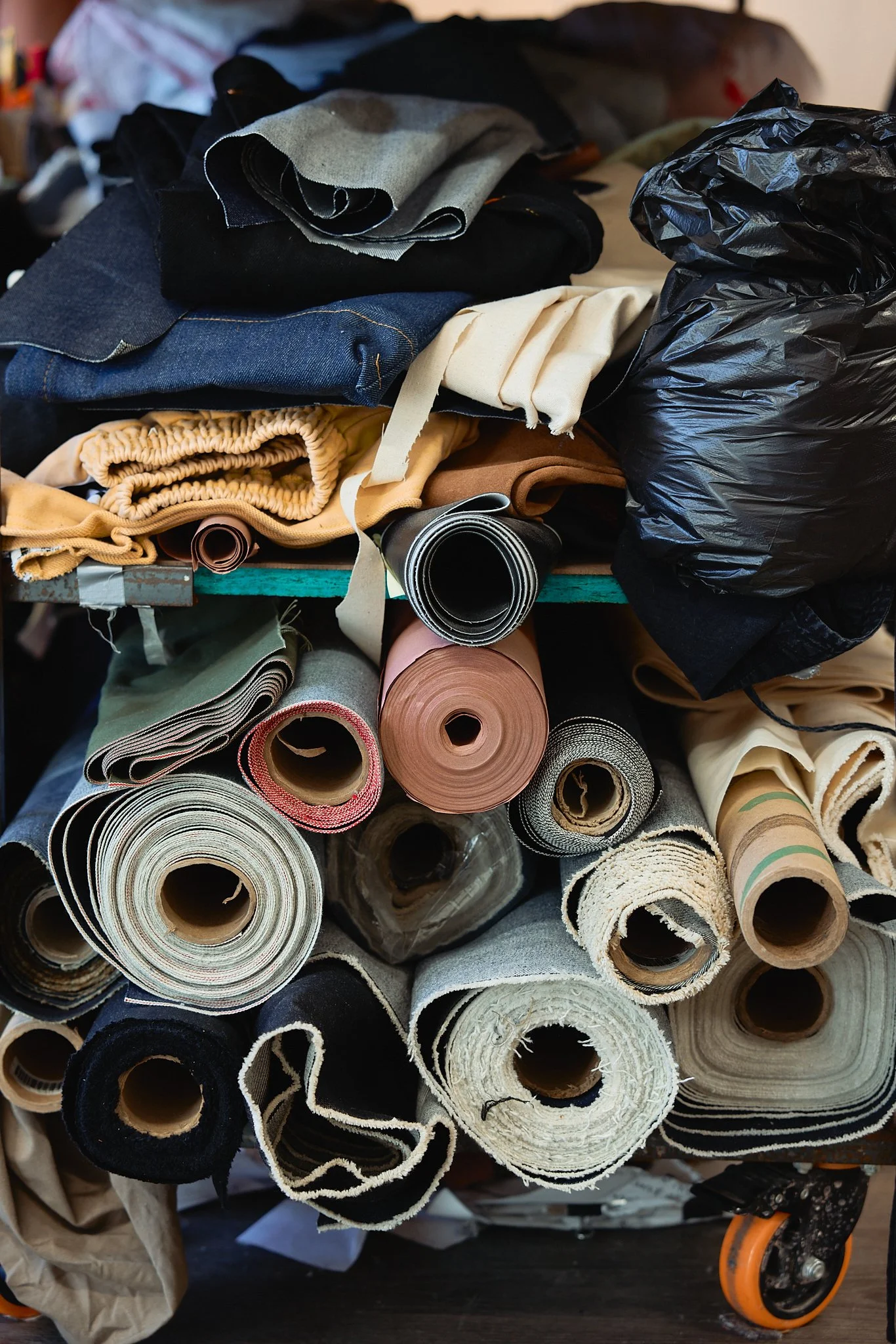 A cart filled with rolled fabrics, textiles, and a black plastic trash bag.