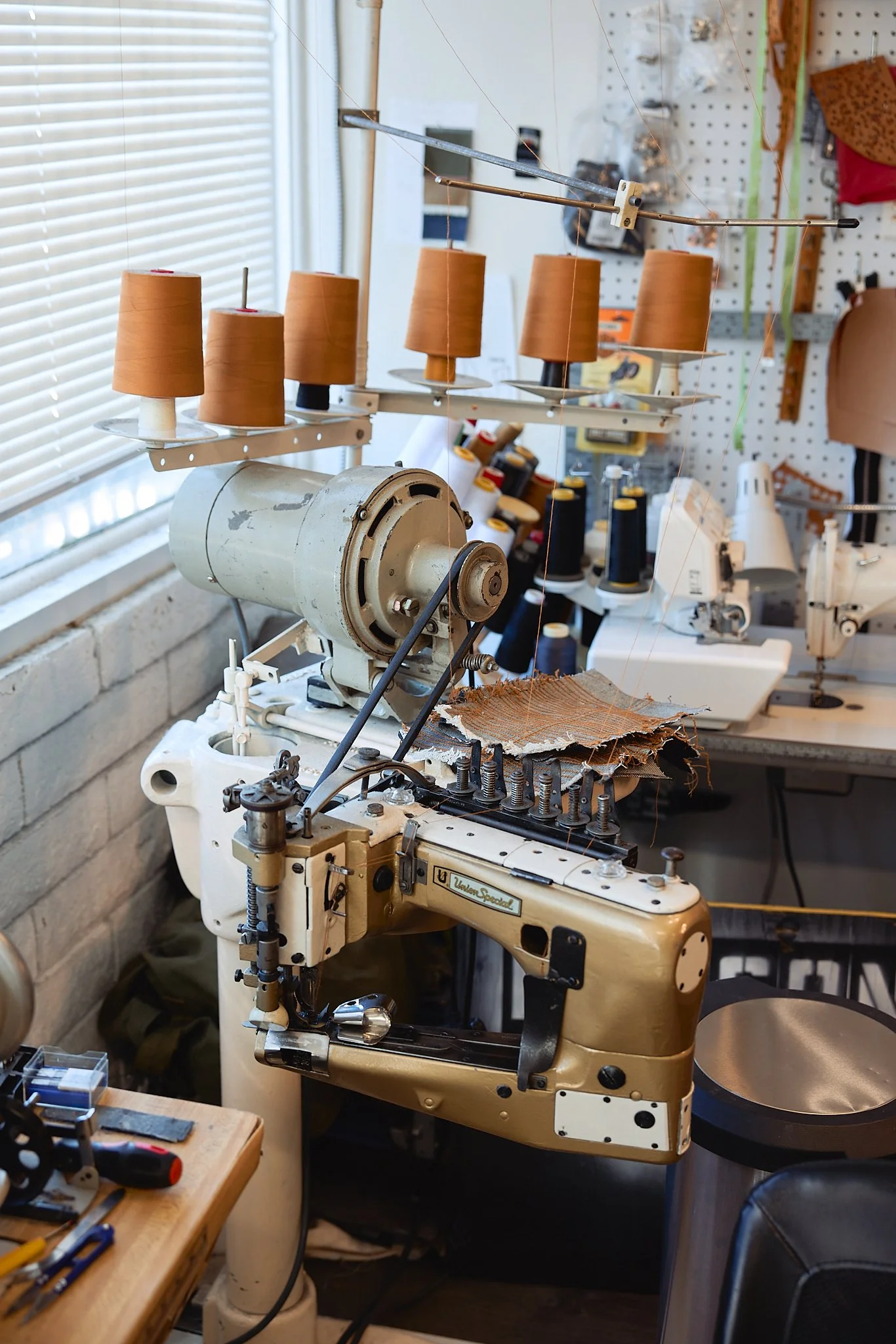 A vintage sewing machine in a workshop surrounded by spools of thread, fabric, and tools.