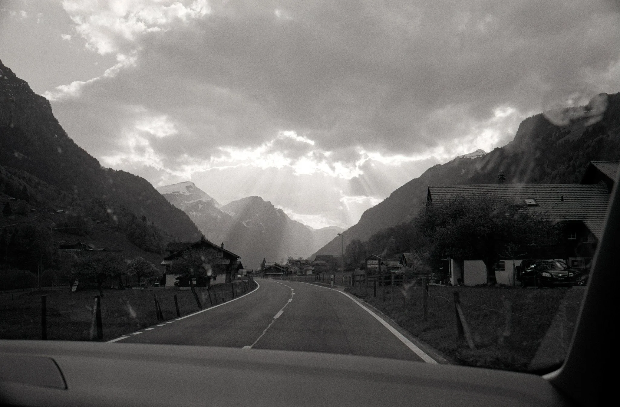 Black and white photo of a mountainous landscape with a winding road, houses, and a cloudy sky.