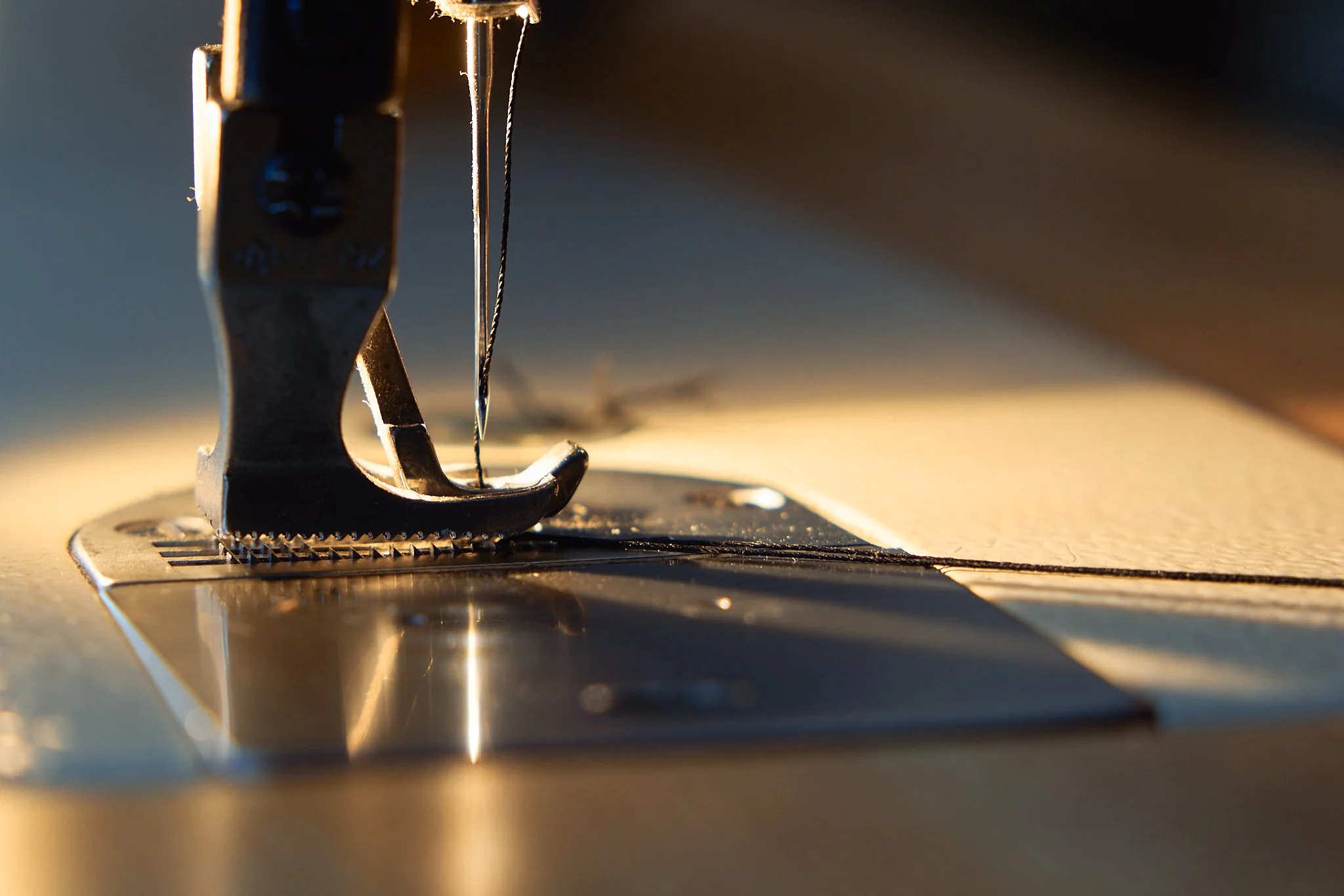 Close-up of a sewing machine needle and foot stitching fabric with warm lighting.