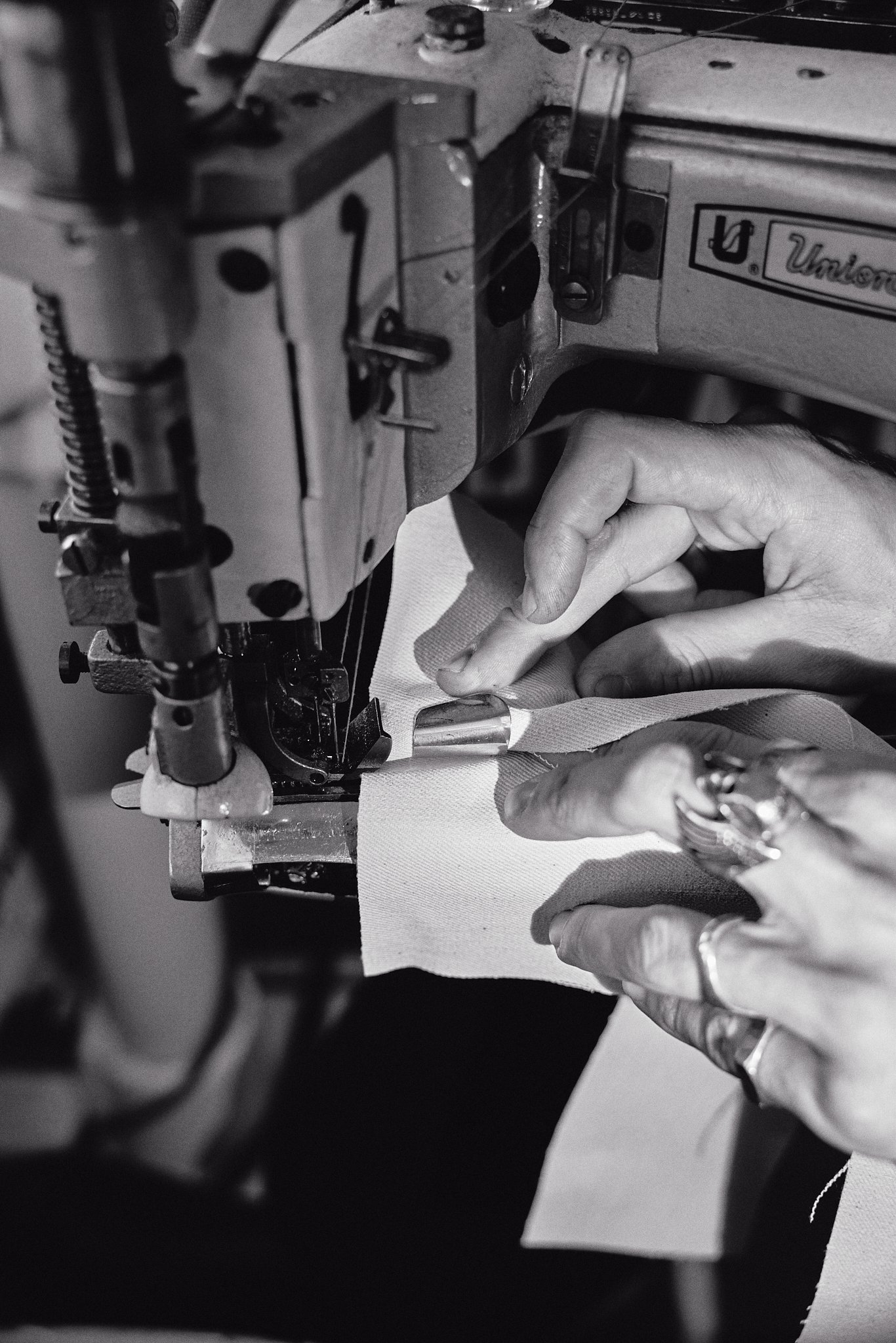 Close-up of sewing machine stitching fabric, with person's hands guiding fabric through the machine.