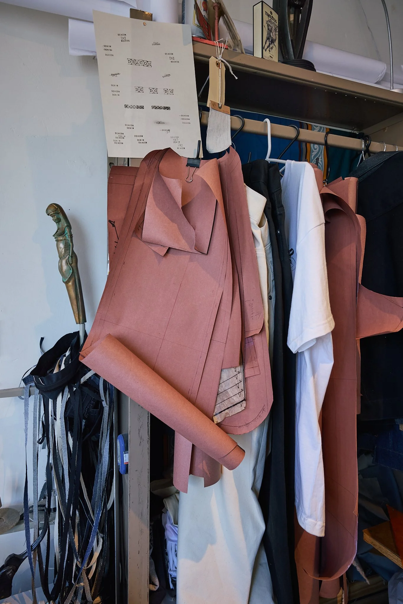 Clothing and fabric patterns hanging on a rack with design sketches on the wall behind.