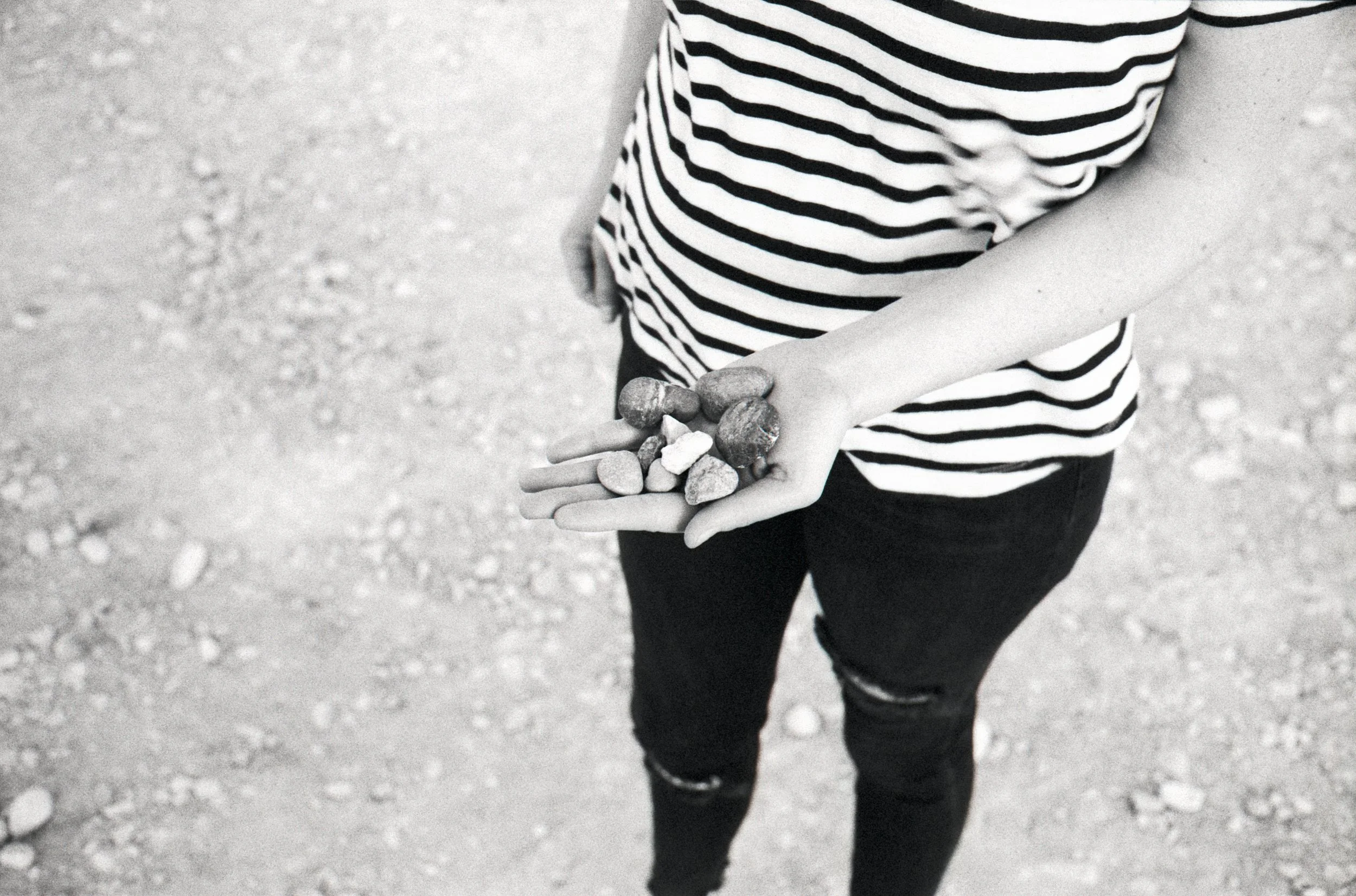 Person wearing a striped shirt and ripped jeans holding a handful of small rocks