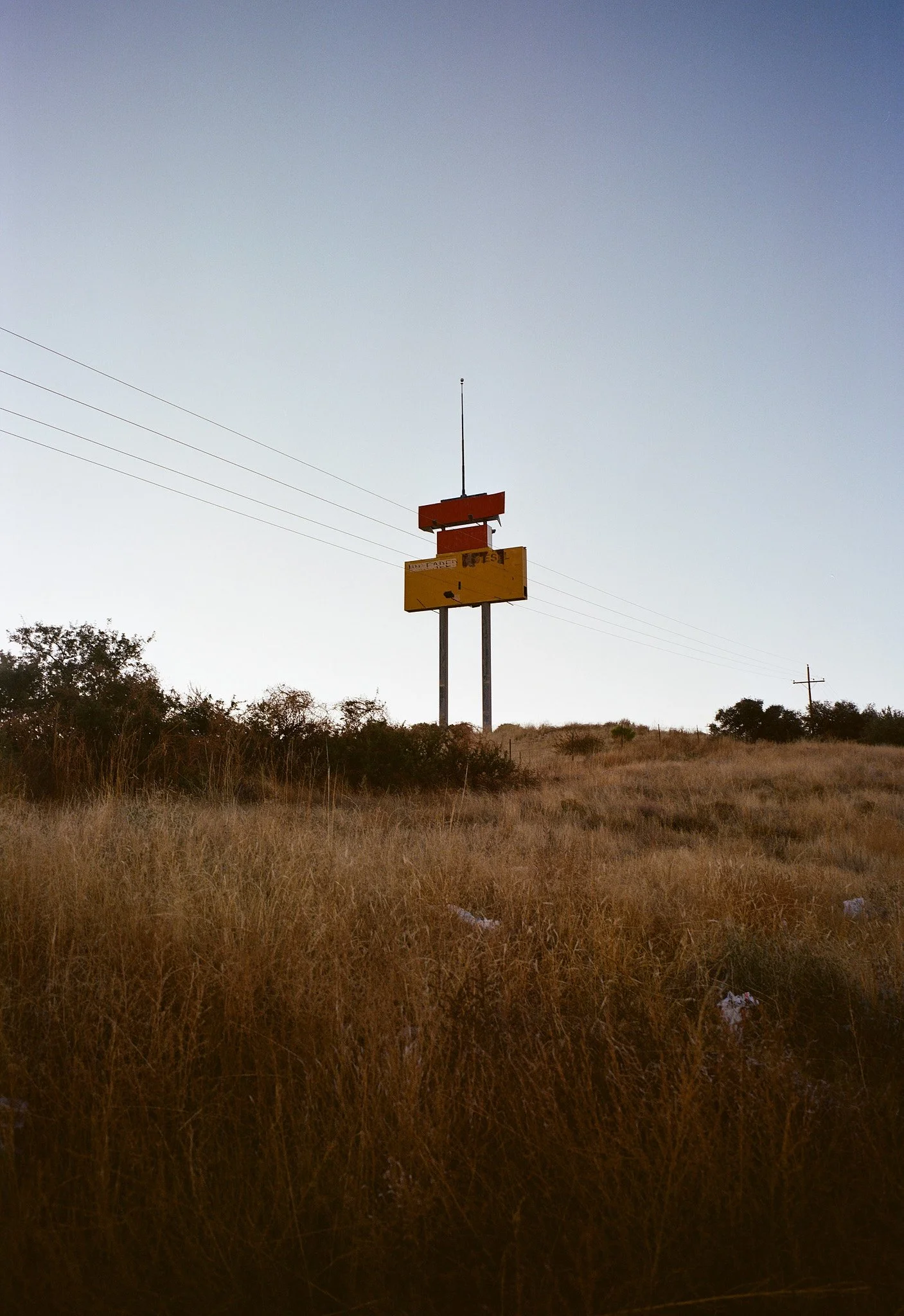 A roadside scene with a tall, empty billboard on metal poles in a grassy field under a clear sky.