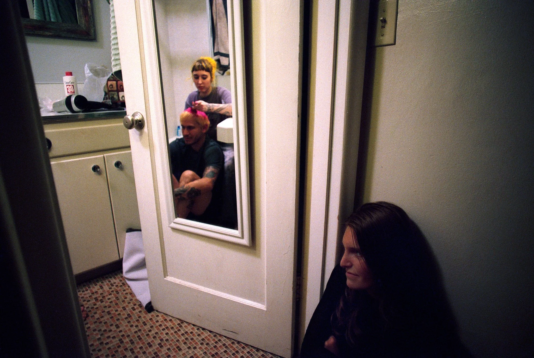 People sitting on the floor of a room, through a mirror on the door, with a woman resting against the wall outside.