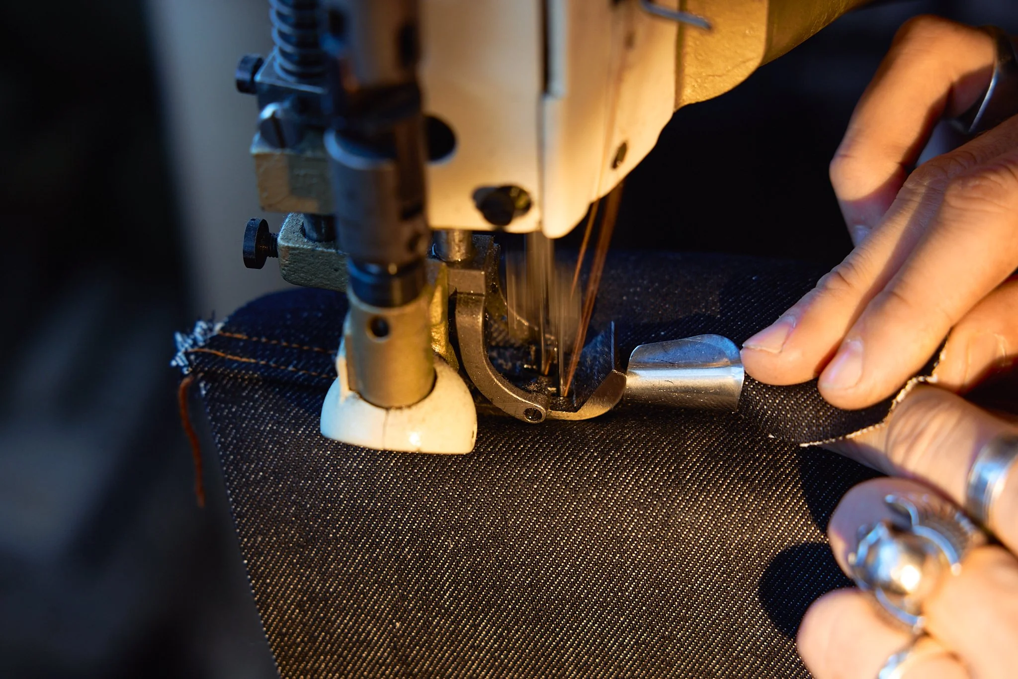 Close-up of a person sewing black fabric with a sewing machine, with hands guiding the fabric.