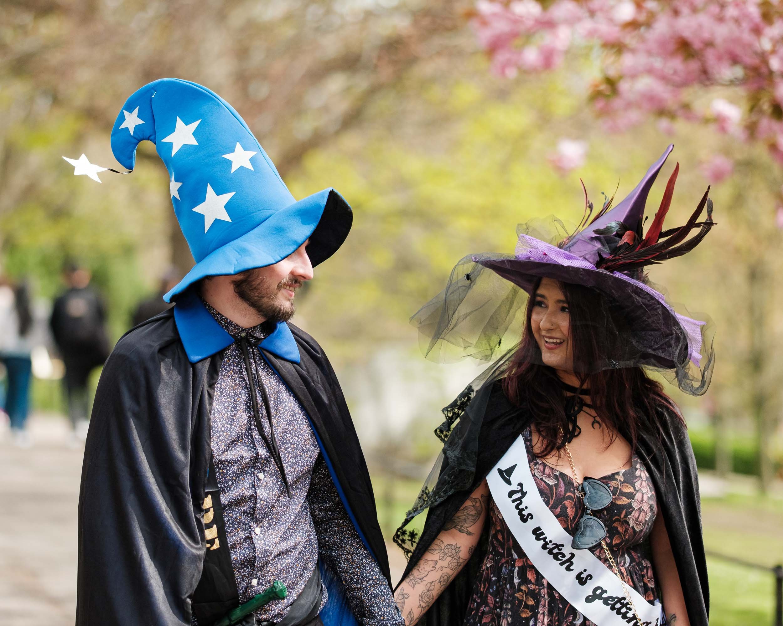 A man and woman dressed as wizards in a park, wearing colorful witches and wizard hats.