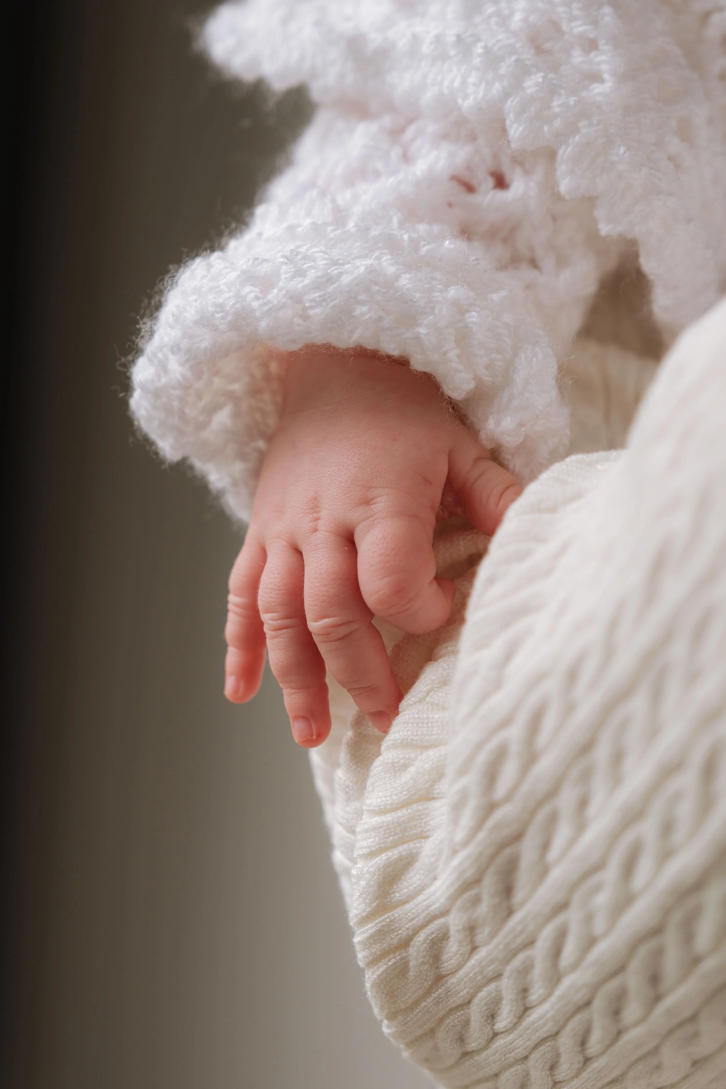 Close-up of a baby's tiny hand gripping a soft, textured blanket, wearing a fluffy white sweater.