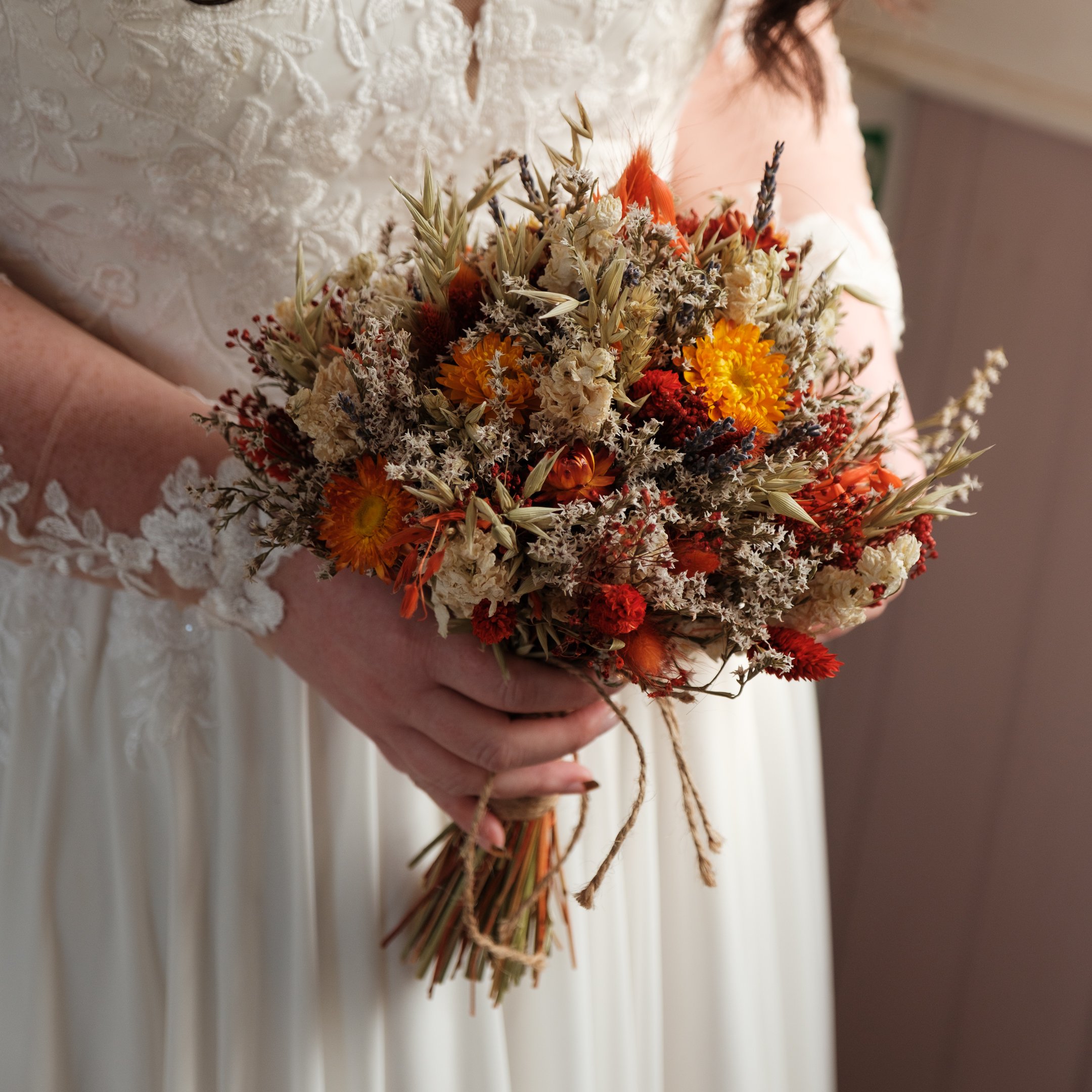 A bride holding a bouquet of dried flowers in shades of orange, red, cream, and beige in Edinburgh.