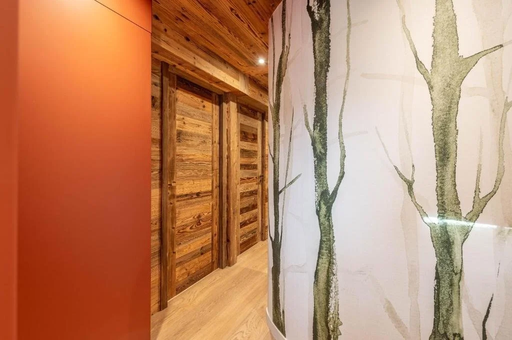Mur peint avec un motif d'arbres stylisés vert foncé sur fond beige, murs en bois rustique et sol en bois naturel.
