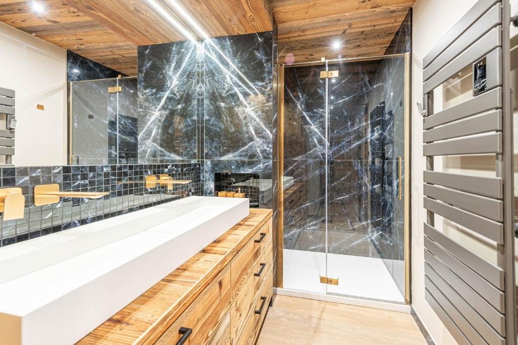 Salle de bain moderne avec lavabo rectangulaire blanc, murs en marbre noir, cabine de douche en verre avec carrelage en marbre noir, mobilier en bois naturel et sèche-serviettes en métal gris.