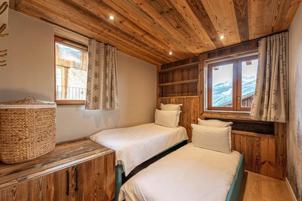 Chambre avec deux lits simples, fenêtres avec vue sur des montagnes, décoration en bois.