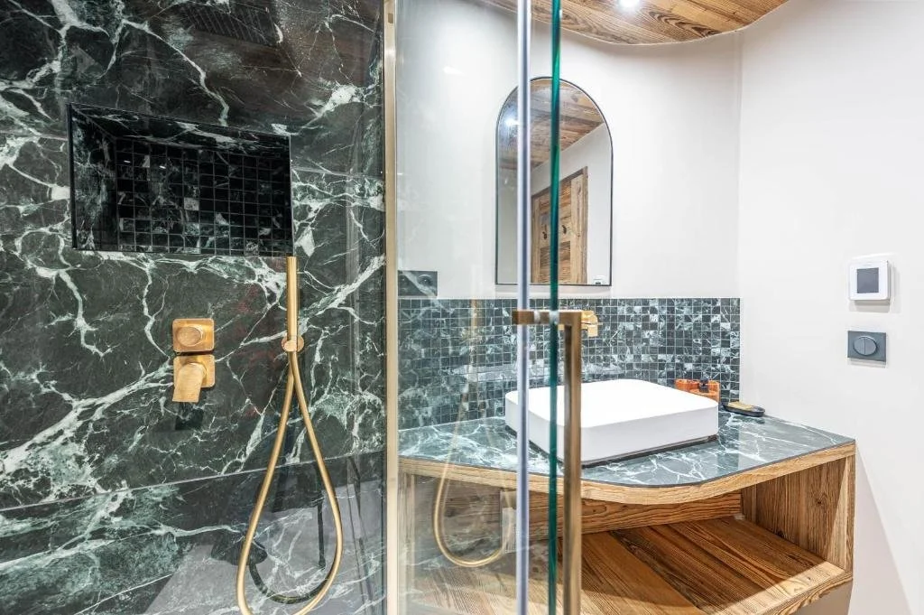 Salle de bain moderne avec une douche en marbre vert avec niche, un lavabo carré en marbre, un miroir arrondi, et un mur blanc.