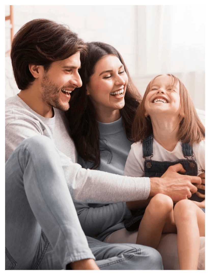 A family of three, two adults and a young girl, laughing and enjoying their time together indoors.