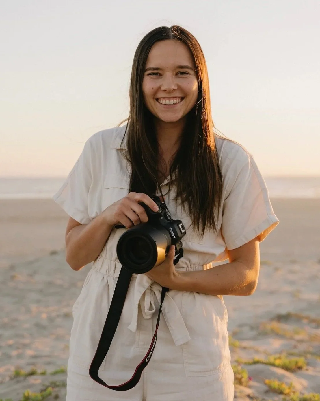Woman smiling on the beach holding a Canon camera