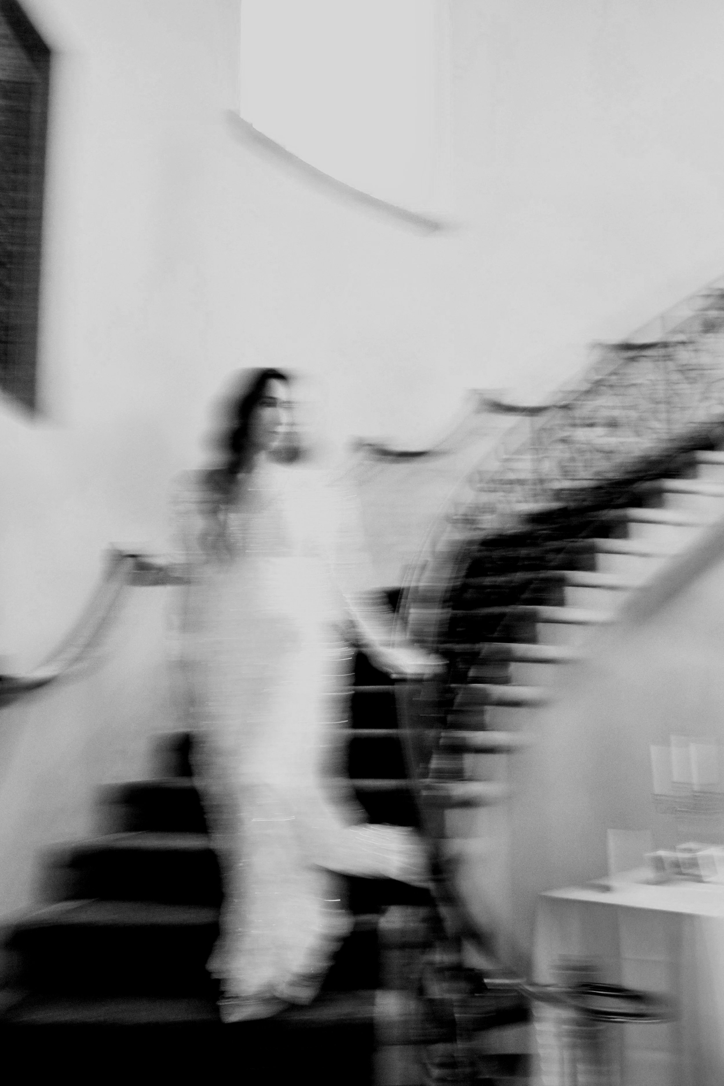 A blurred black and white photo of a woman standing on a staircase.