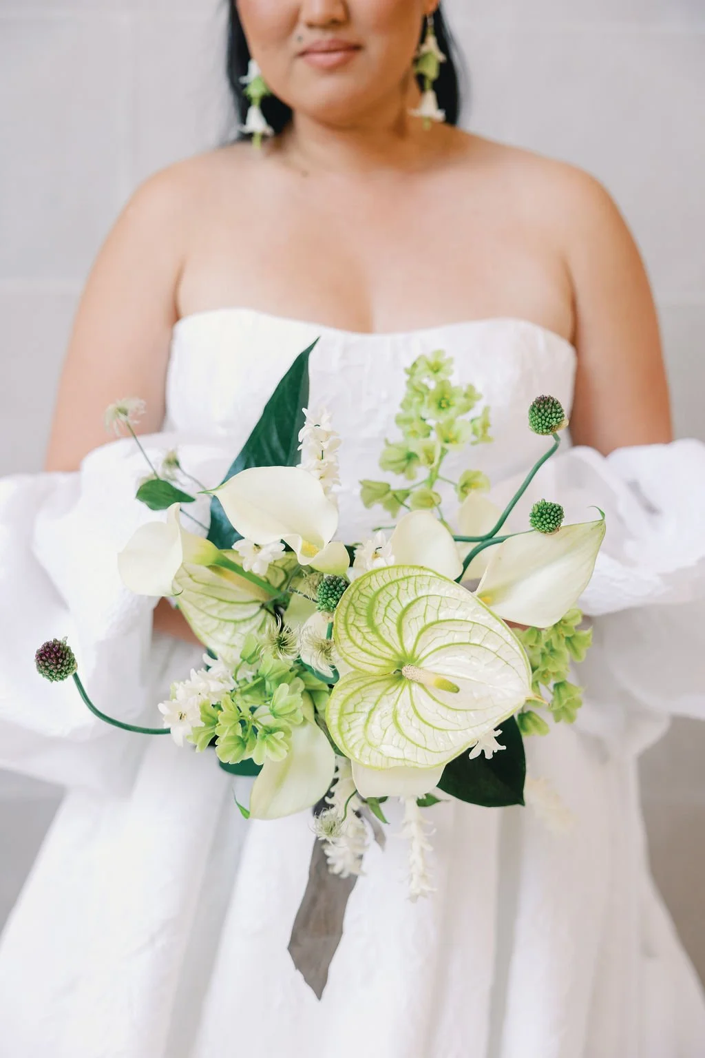 Woman in white strapless dress holding a bouquet of white and green flowers.