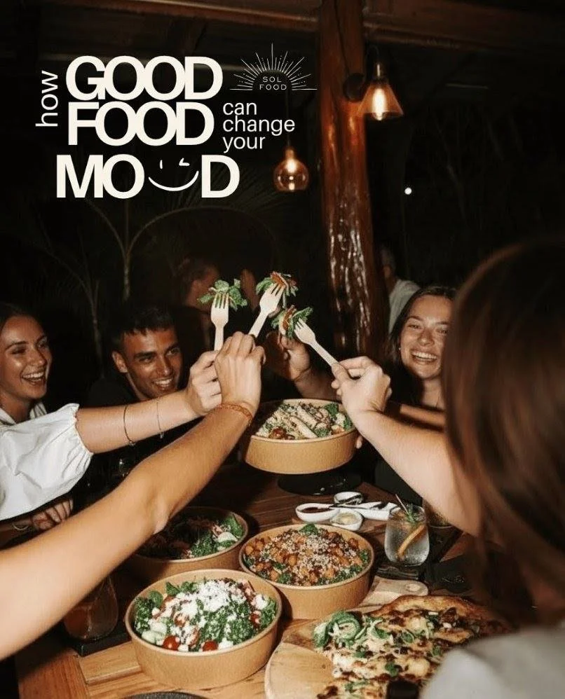 People smiling and raising forks with salads during a dinner, with bowls of pizza and other dishes on the table, in a warm restaurant setting.