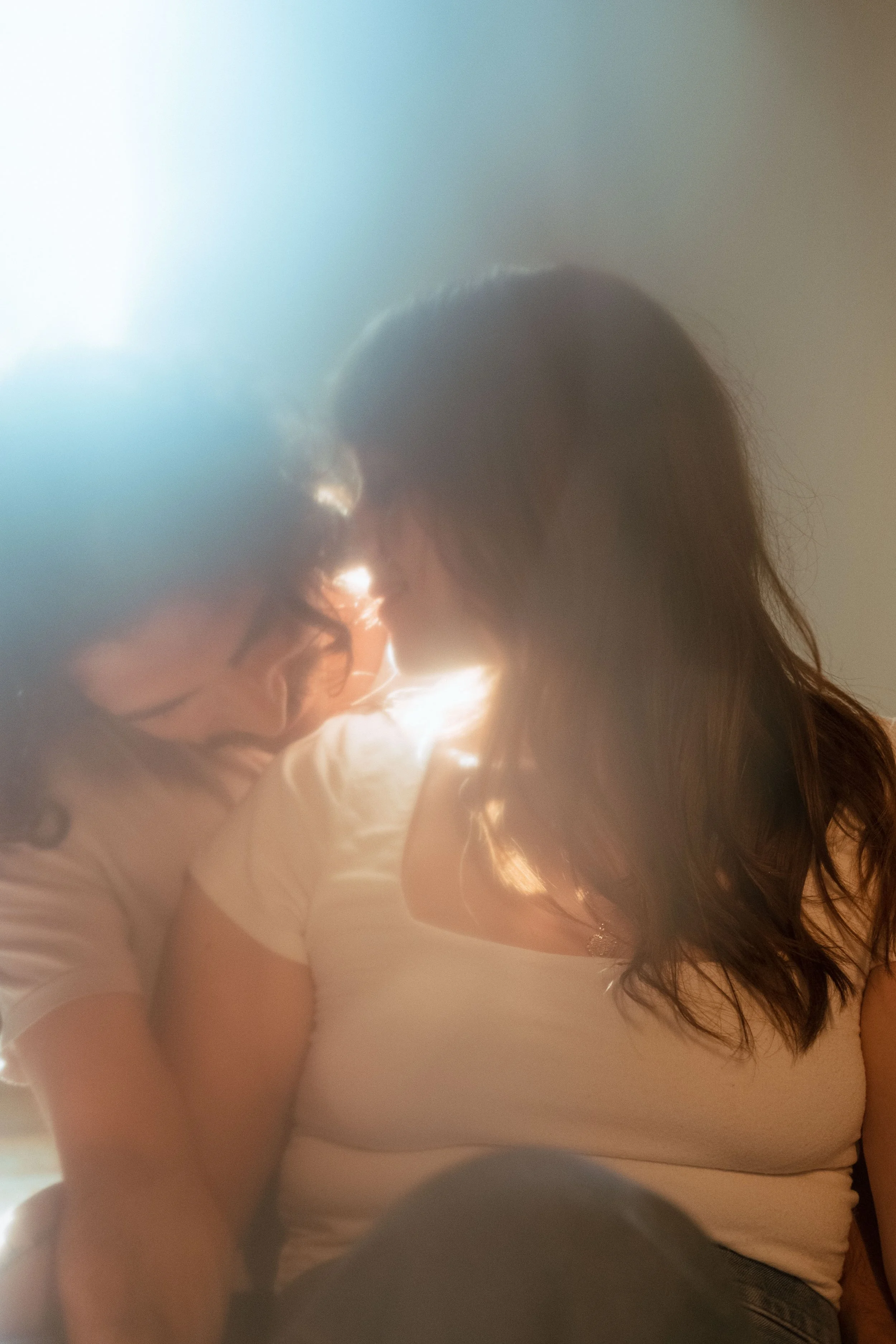 Two women sharing an intimate moment with their foreheads and noses touching, sunlight illuminating the scene.