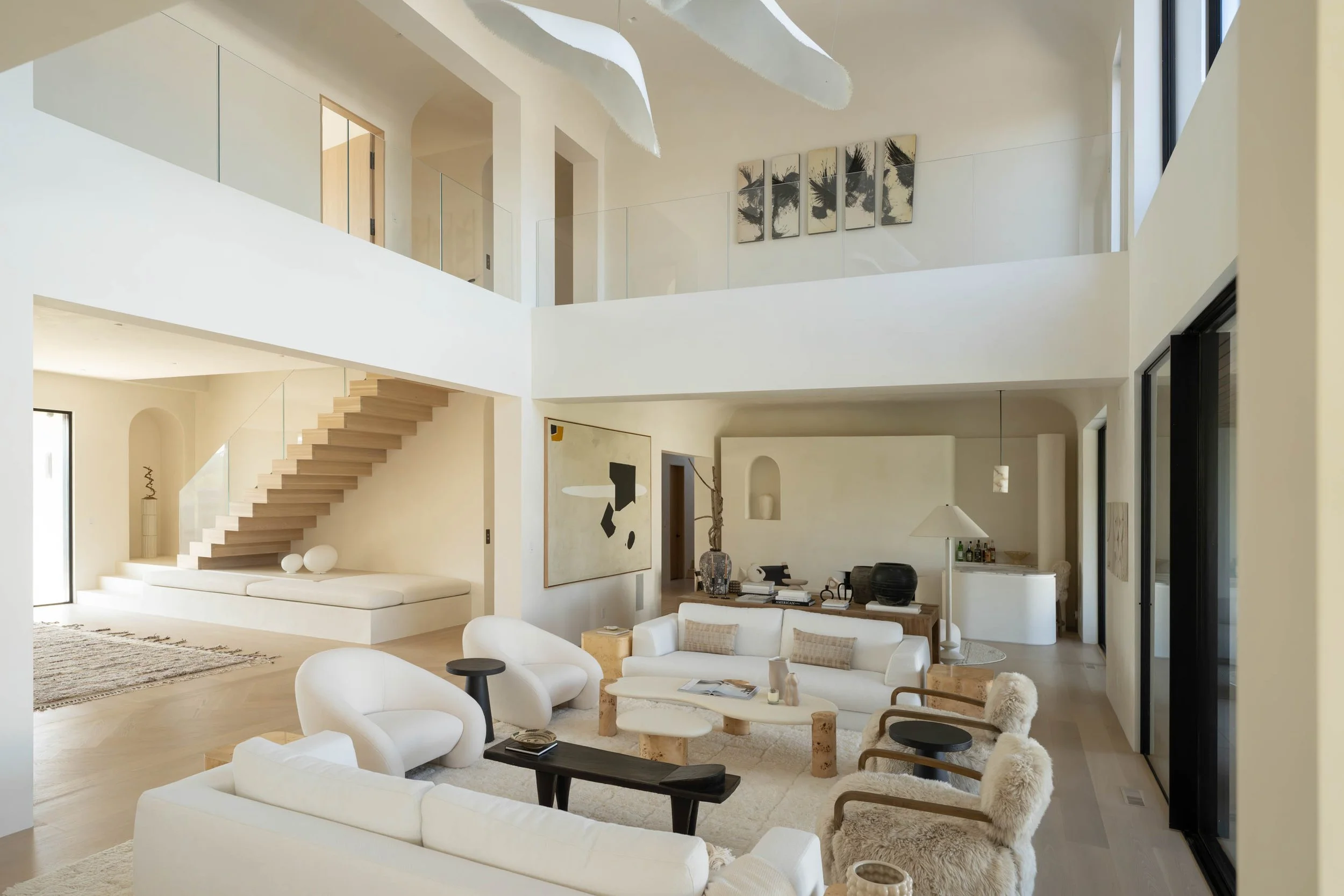 Modern living room with white furniture, minimalistic decor, and a staircase leading to an upper floor.