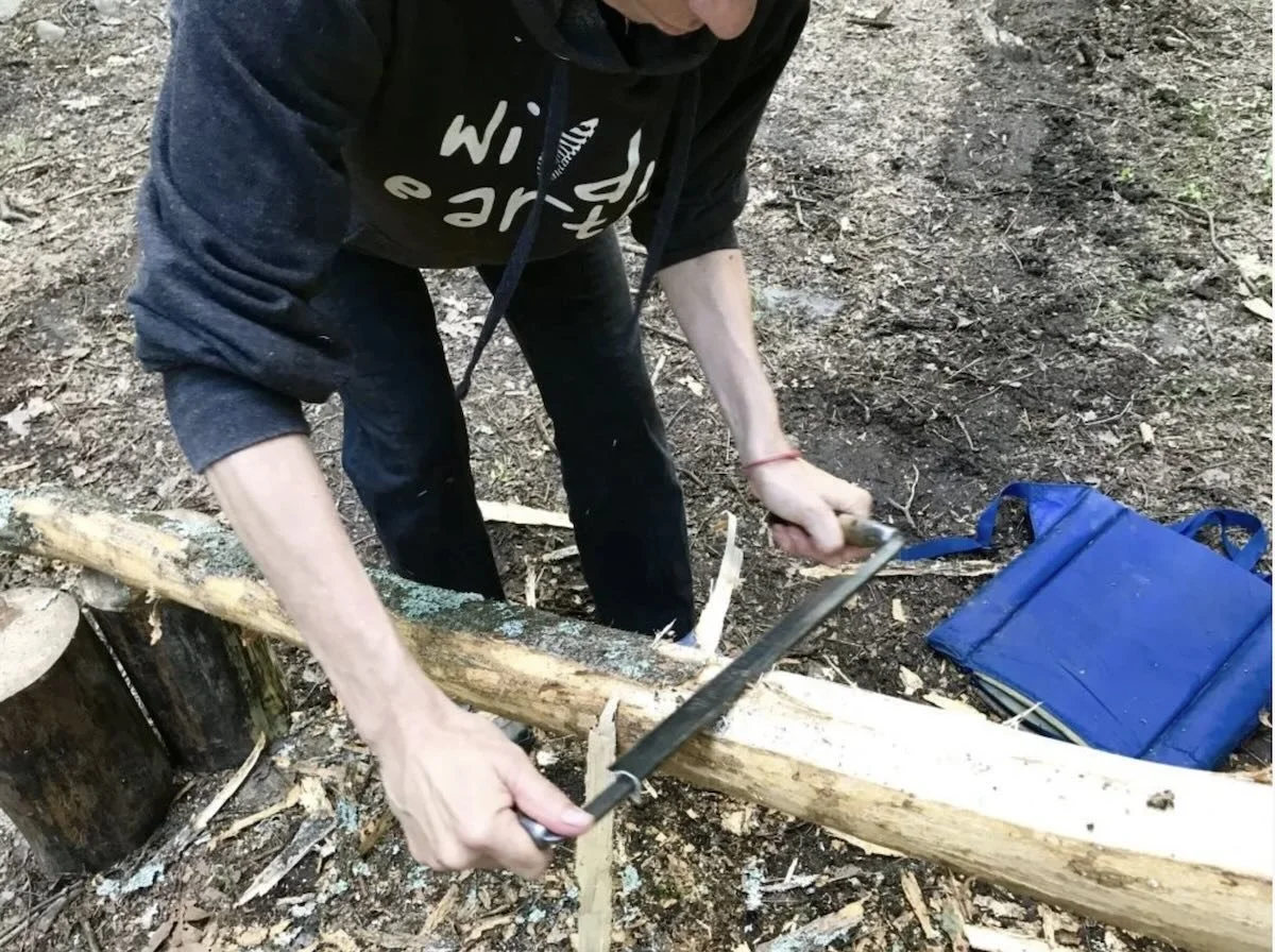 a person using a drawknife to remove bark from a log for basket weaving