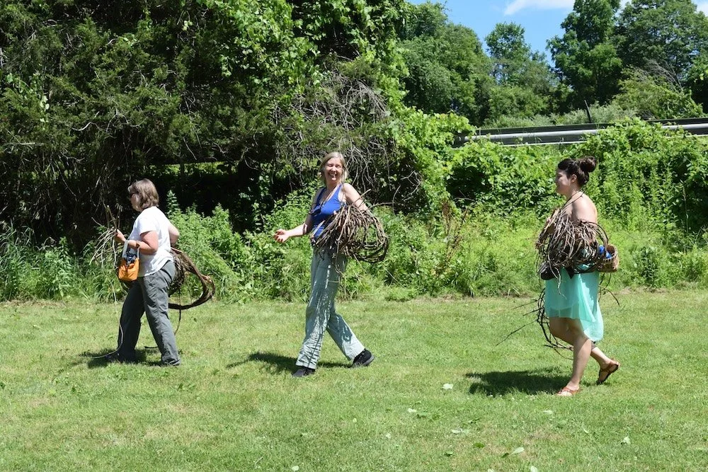 three women strolling with vines for basket weaving in hand
