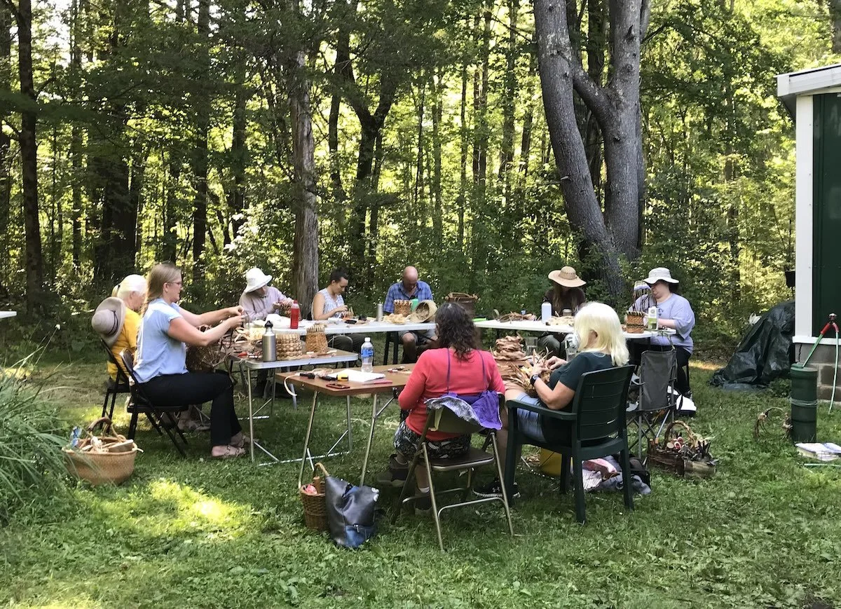 a basket making class sitting around a table weaving