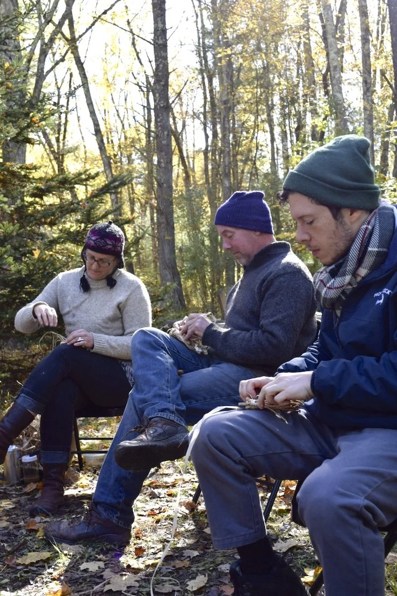 three people sitting around a fire making cordage with plant fibers