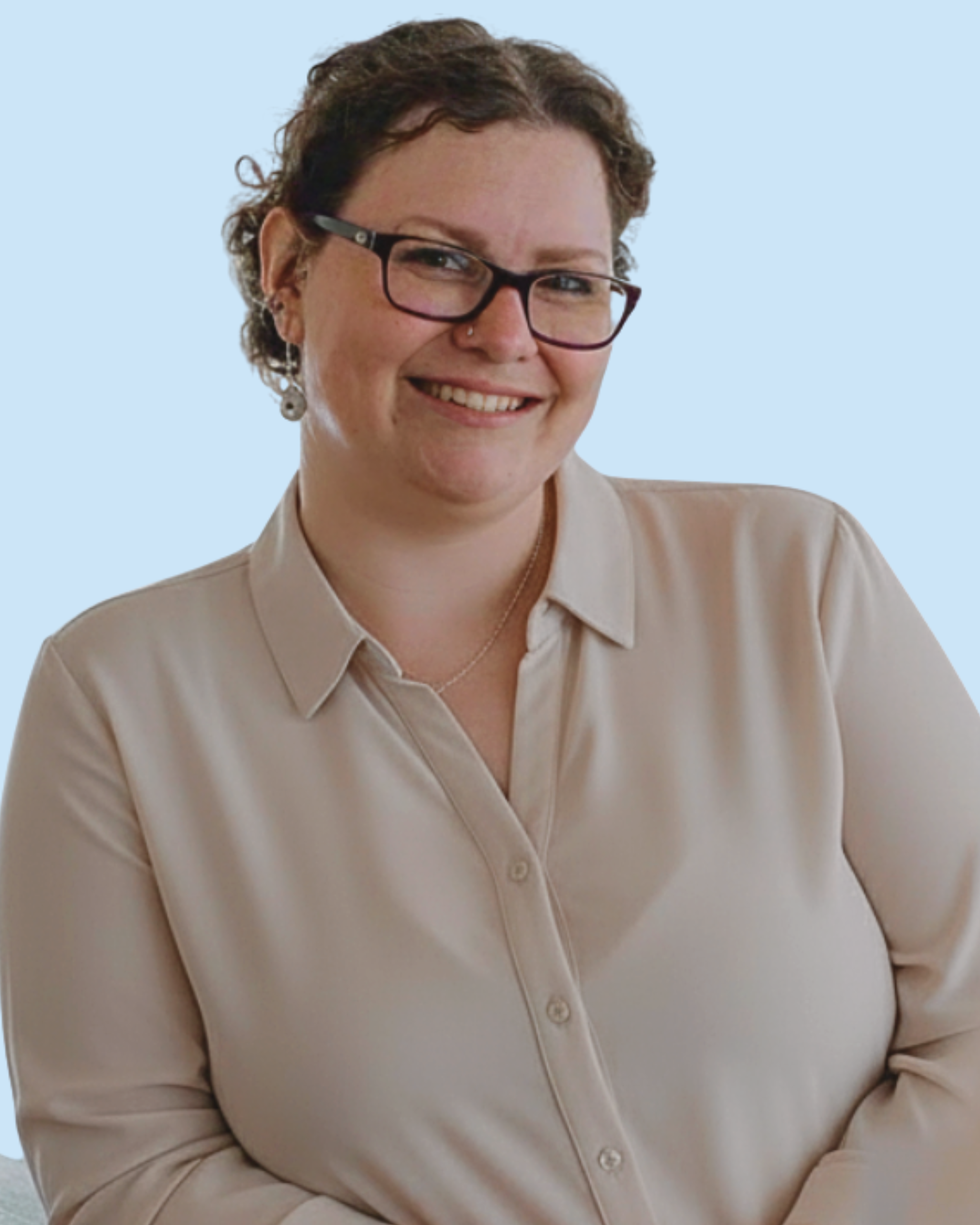 A woman with short curly brown hair, glasses, and earrings, smiling at the camera, wearing a beige button-up shirt, against a light blue background.
