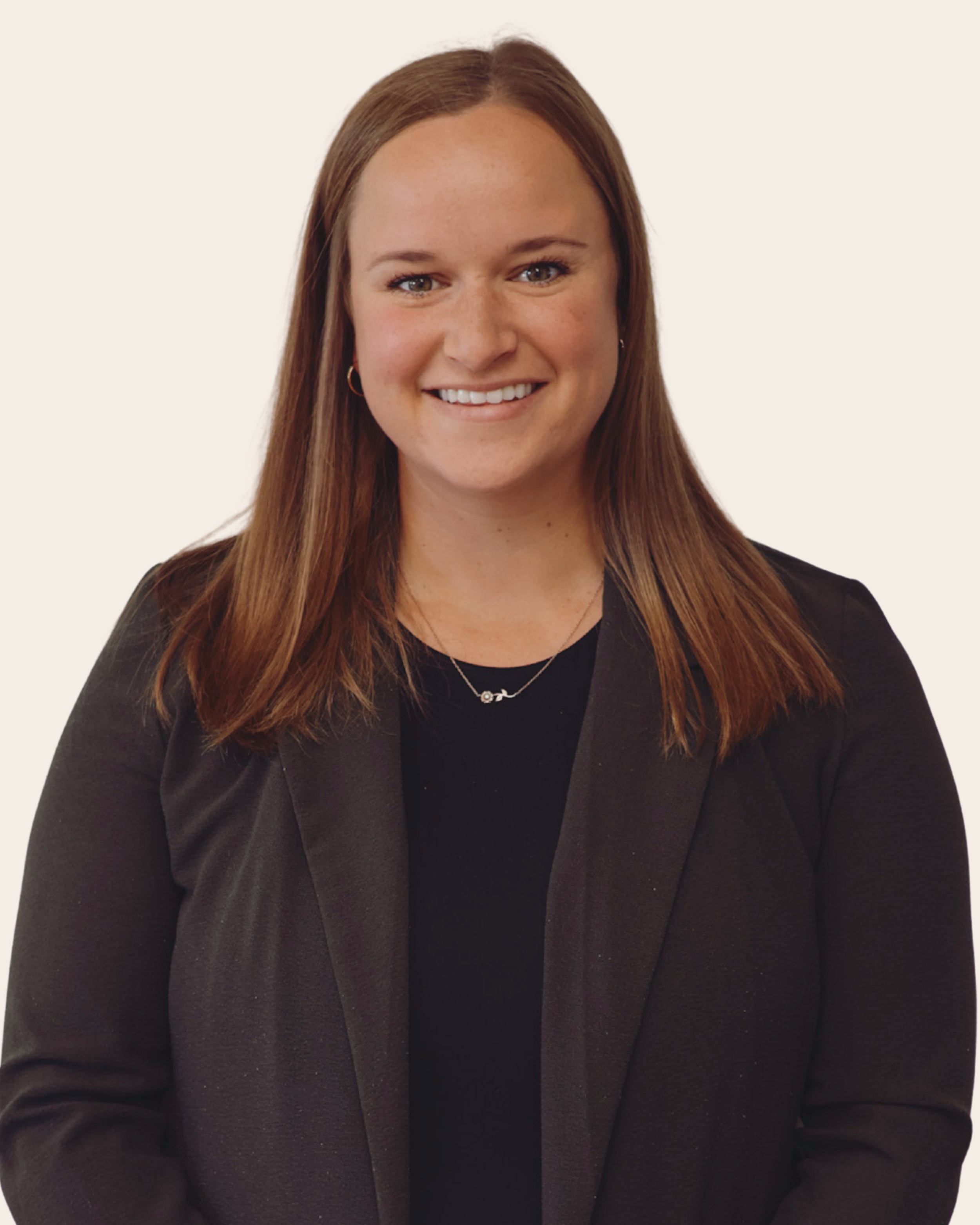 Portrait of a woman with brown hair, smiling, wearing a black blazer and a necklace, against a plain light background.