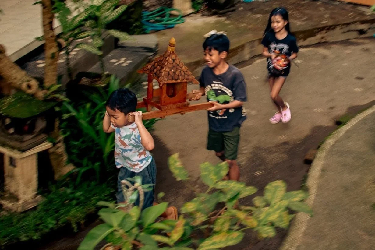 Three children playing with a wooden birdhouse on a tray in an outdoor garden.