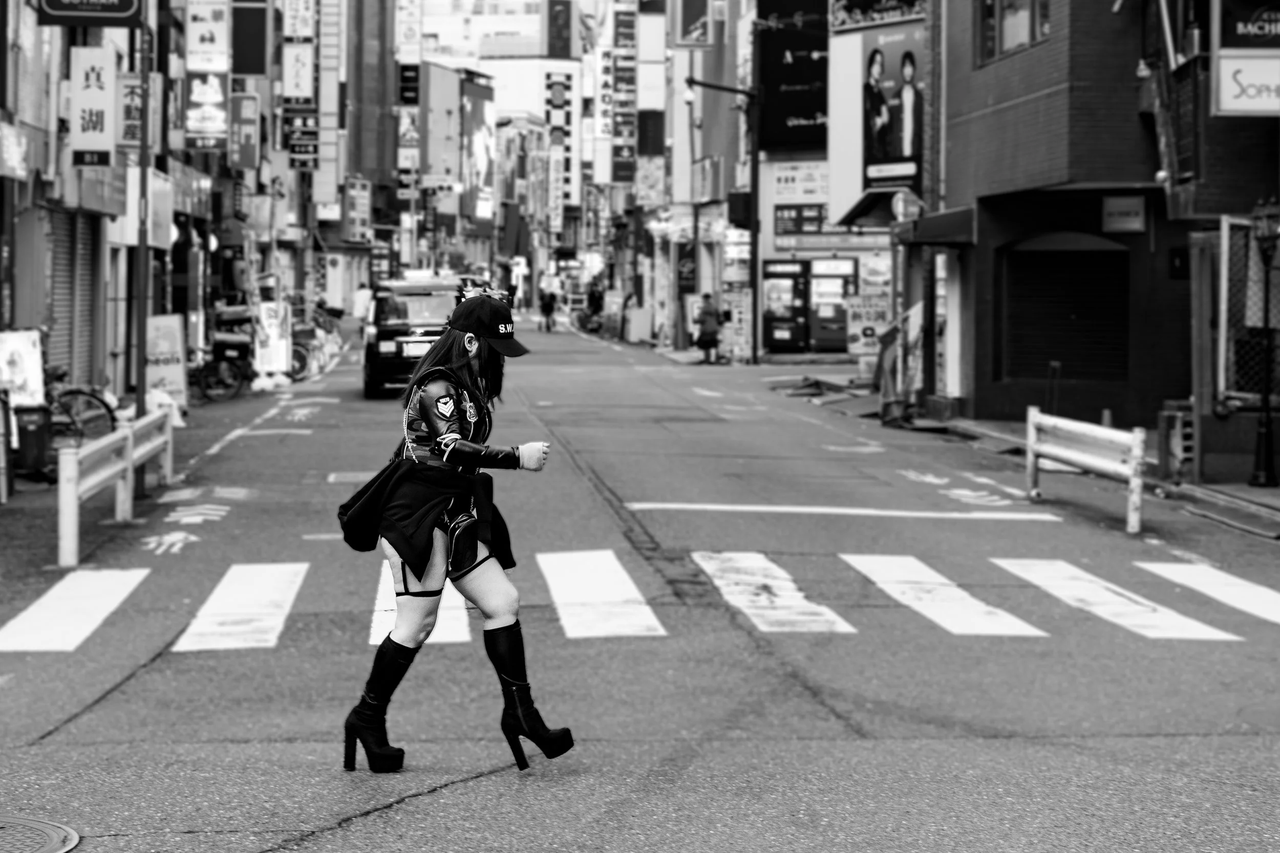 A woman dressed as a police officer with high-heeled boots, walking across a city street in Japan, in black and white.