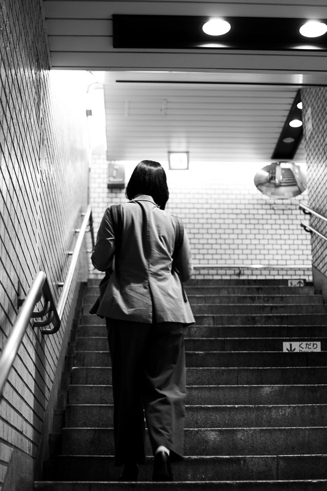 A woman wearing a suit walking up a staircase in an underground or subway station, black and white photo.