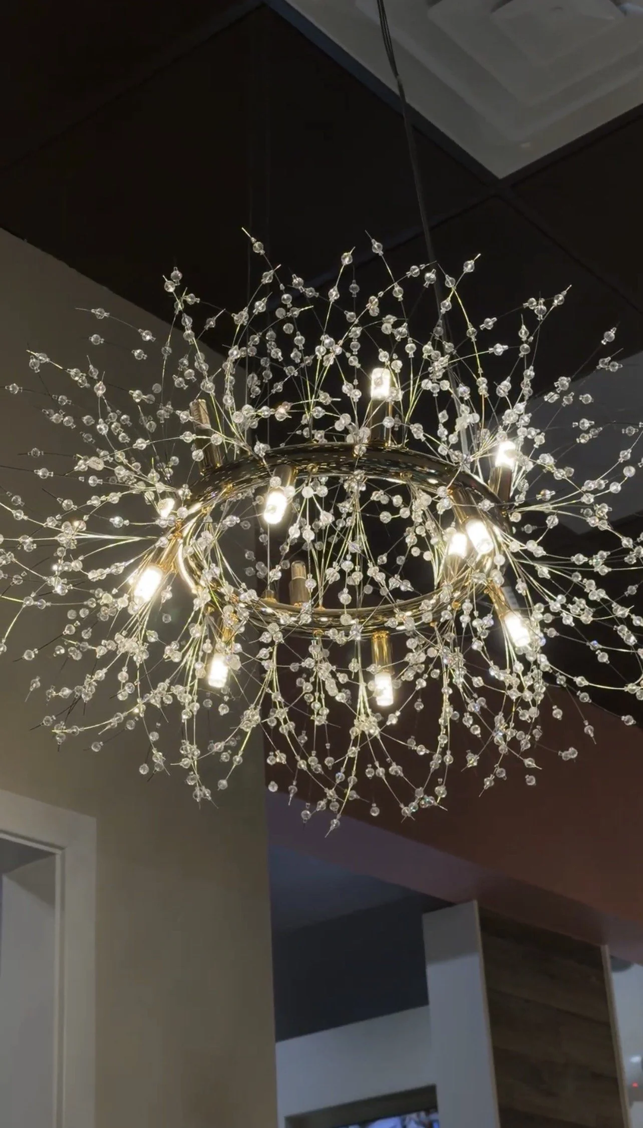 A modern chandelier with a circular metal frame adorned with numerous small crystal beads and multiple light bulbs hanging from the ceiling.