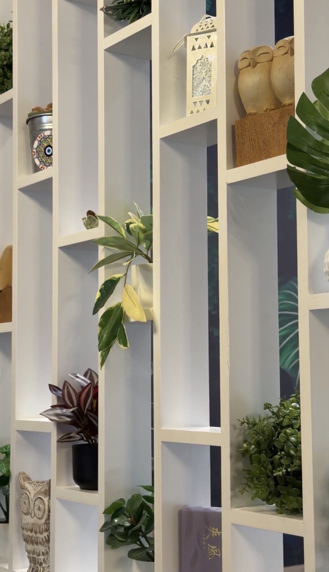 Decorative white shelving unit with various potted plants, vases, and decorative items.