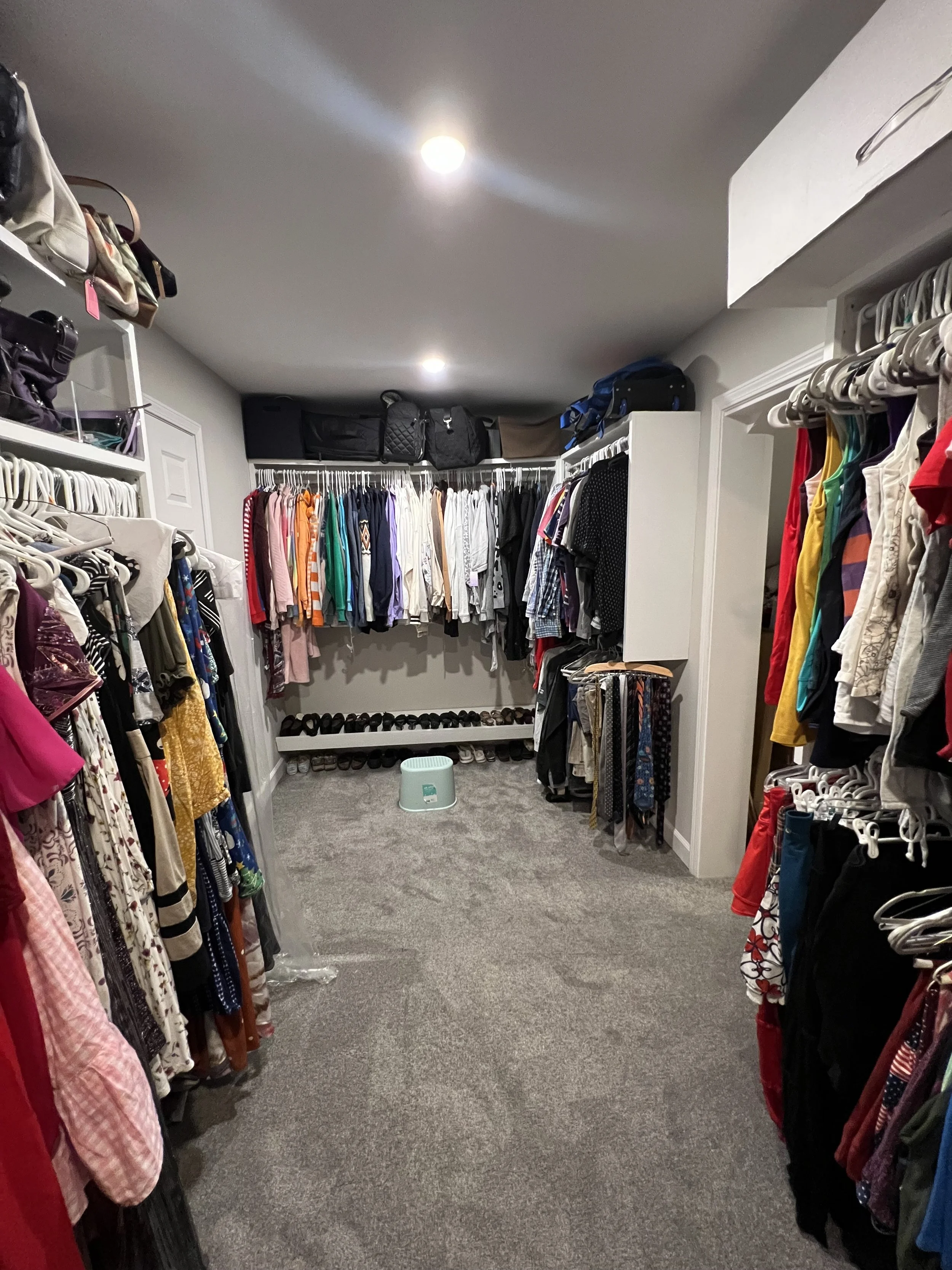 Spacious walk-in closet with hanging clothes, shelves of shoes, and storage bags on top.